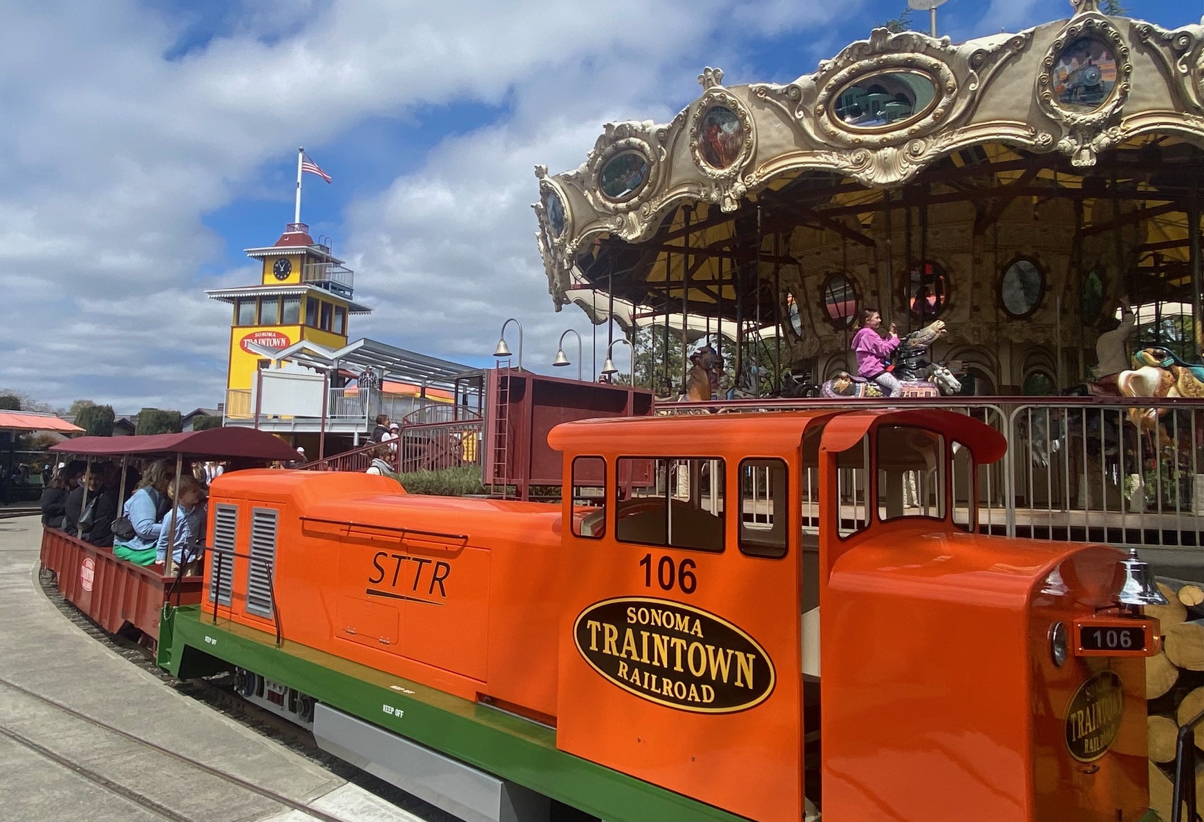 An orange kids' train ride emblazoned with the words &quot;Sonoma Traintown Railroad&quot; is pictured with a carousel in the background.