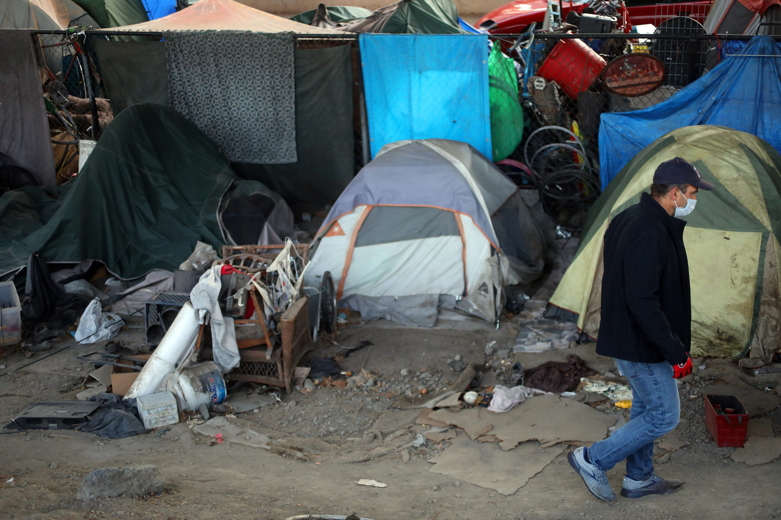 A man in jeans and a jacket passes a row of tents on the street.