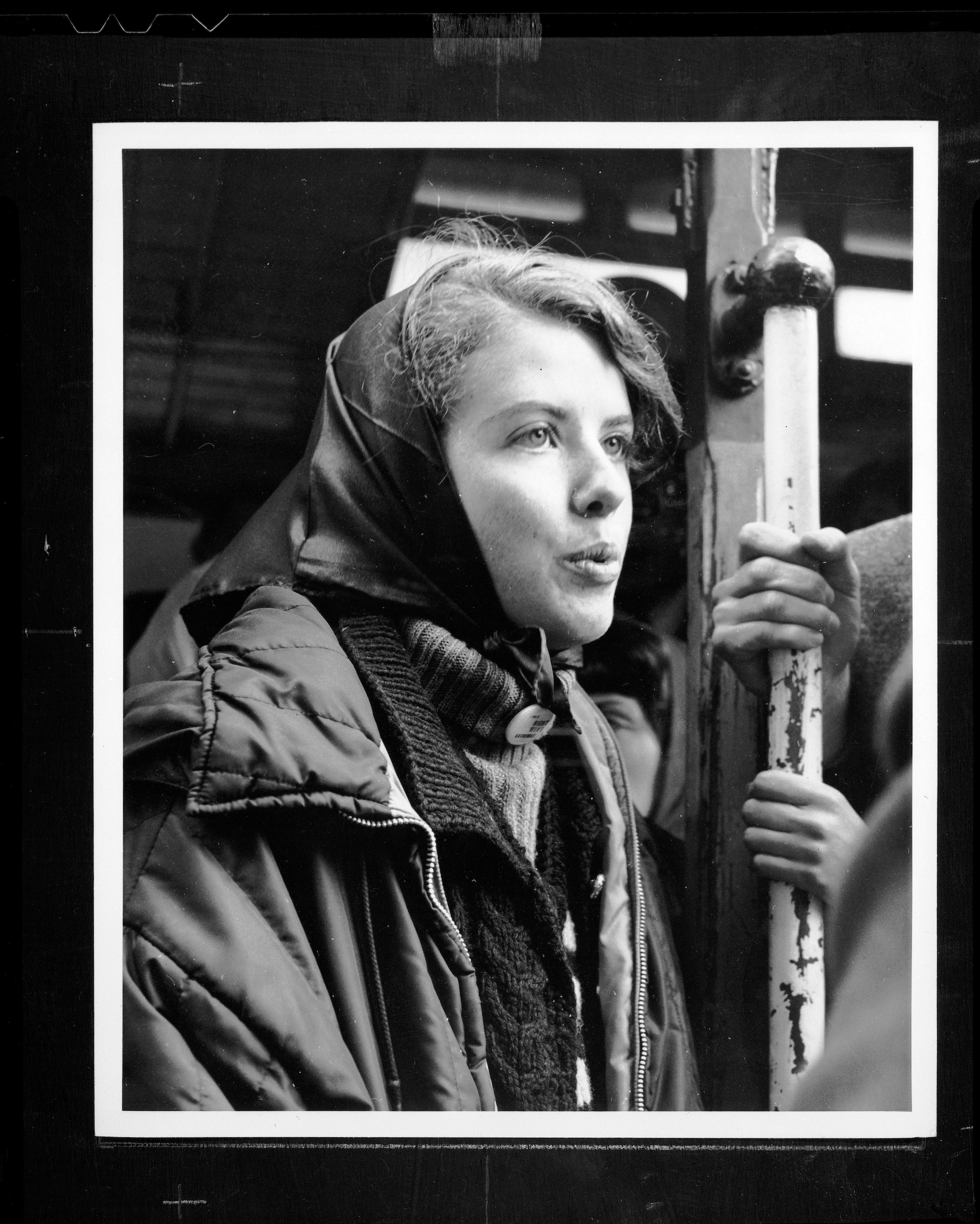 A black and white photo of a woman holding on to a San Francisco cable car.