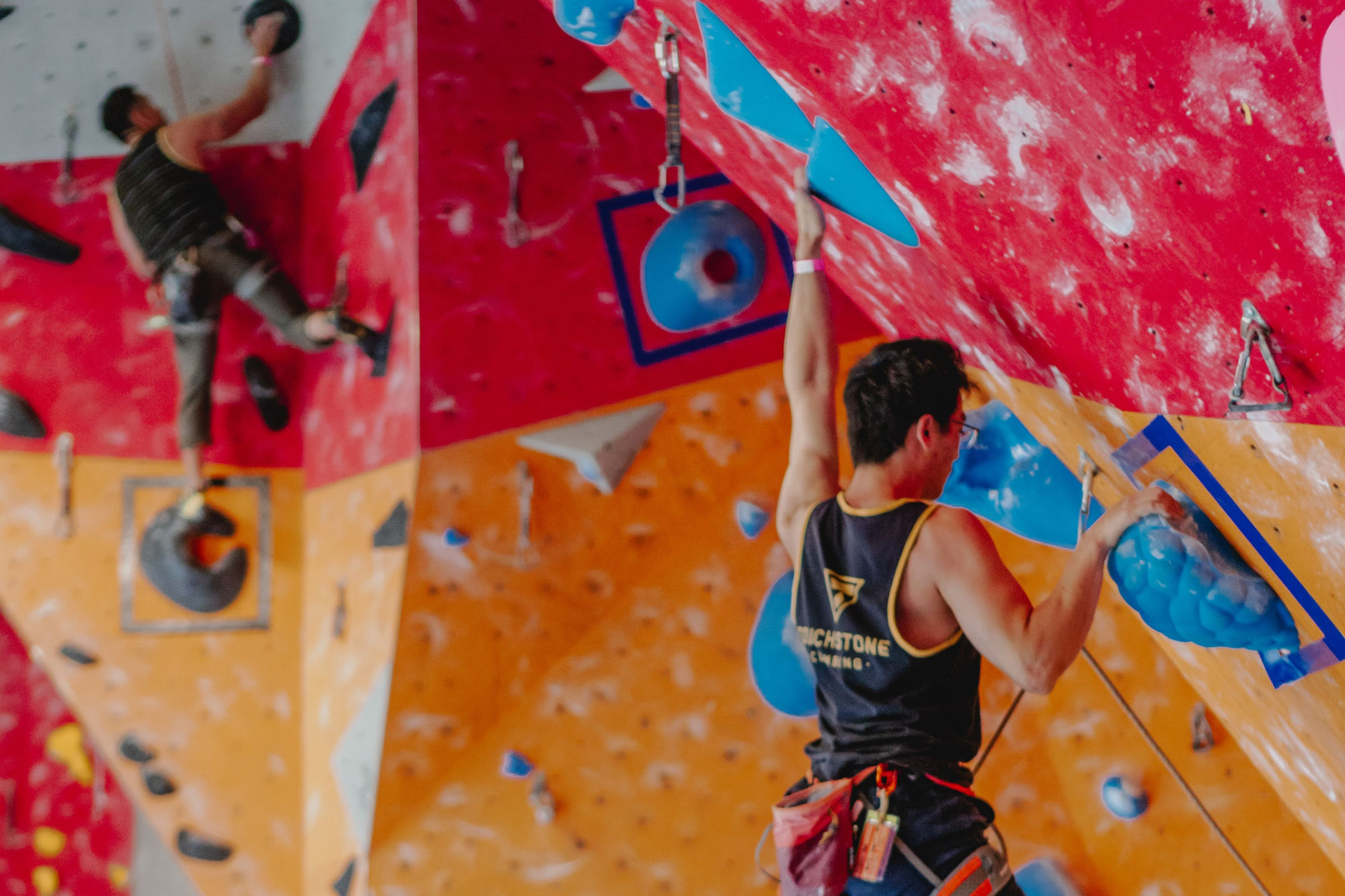 Two men are climbing on a red and orange indoor climbing wall.