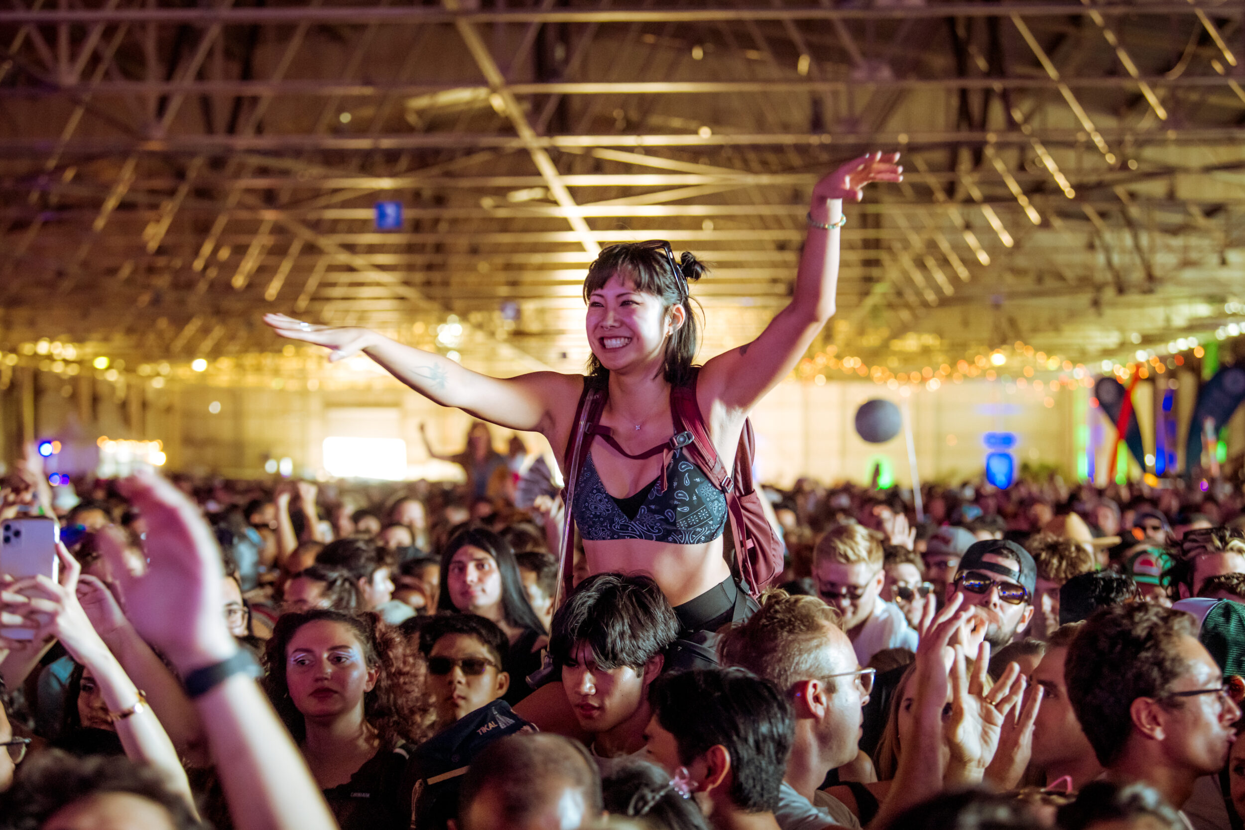 A joyous woman is raised above a crowd at a festival, arms spread wide, smiling.