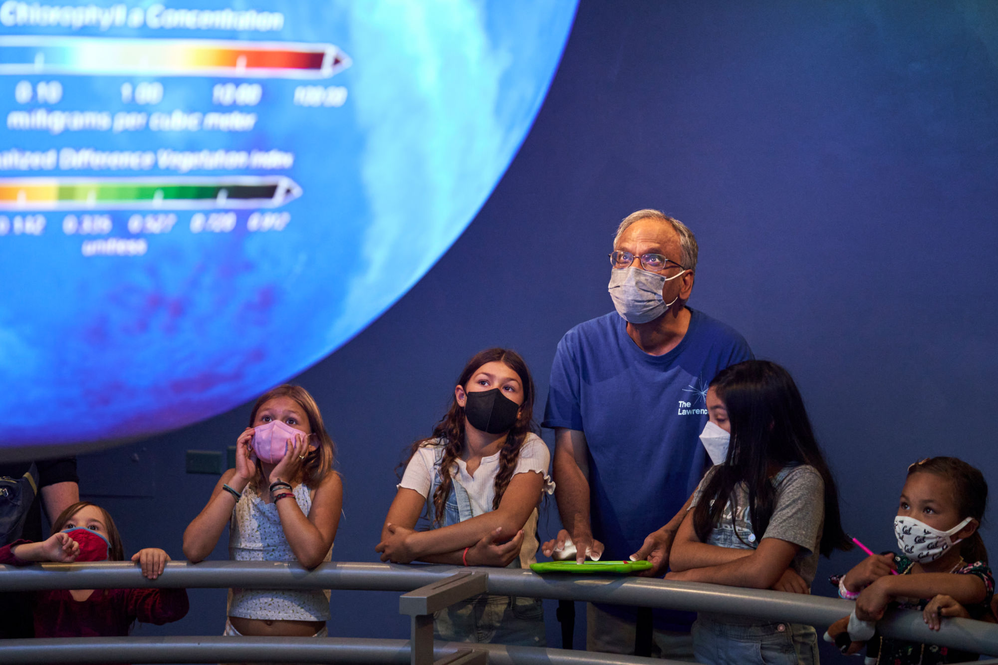 A man teaches kids before a scientific display on a large screen.