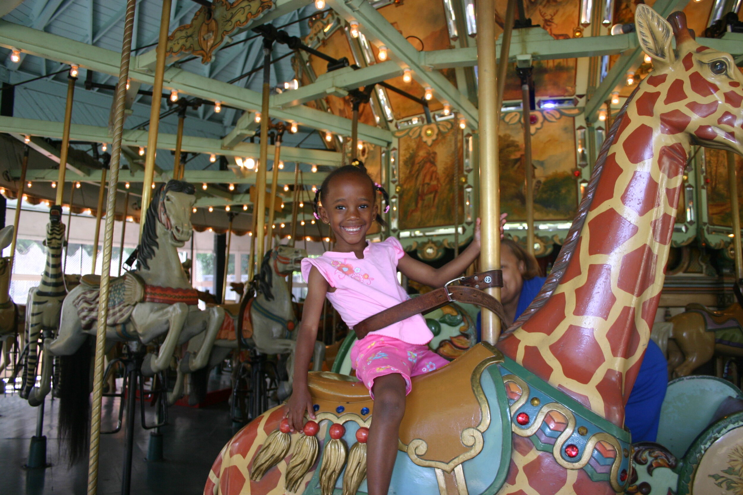 A little girl rides a carousel giraffe.
