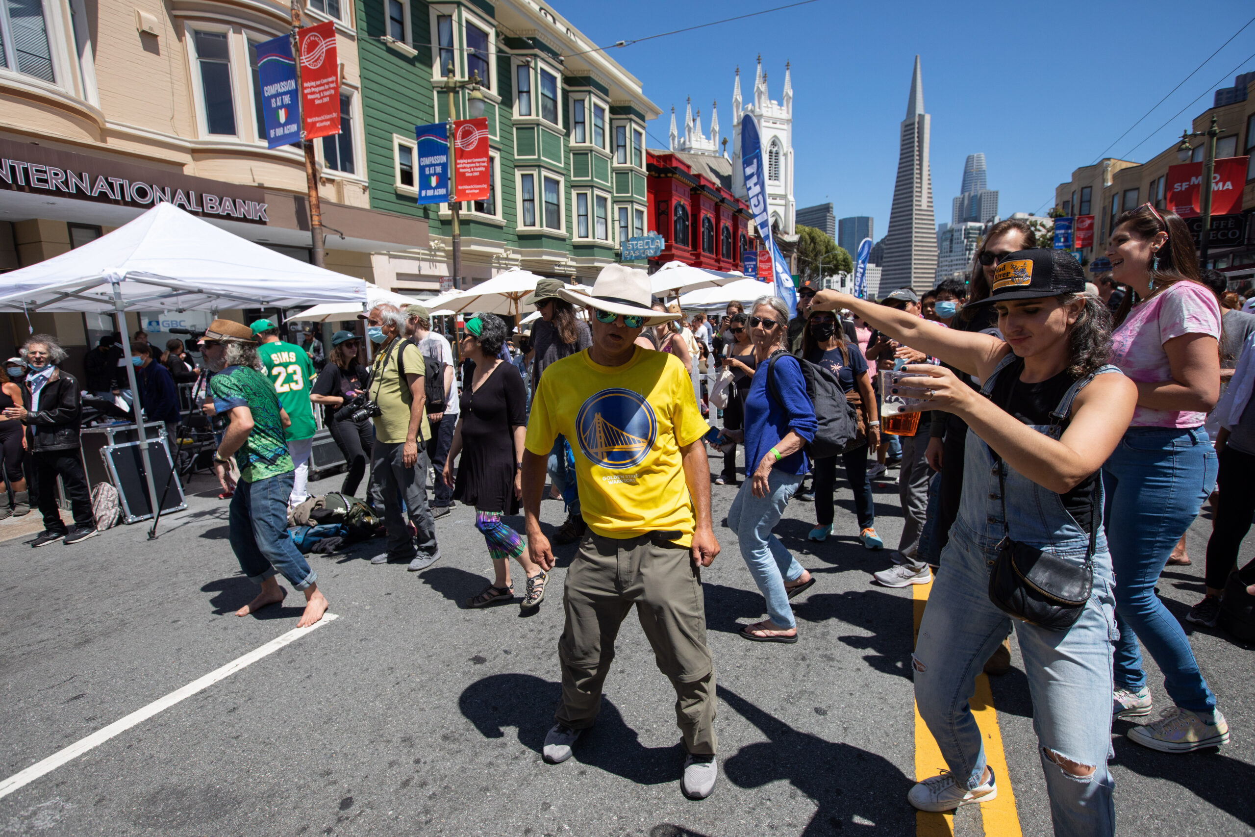 a man shows off his moves in the street during a festival, with the Transamerica pyramid behind him