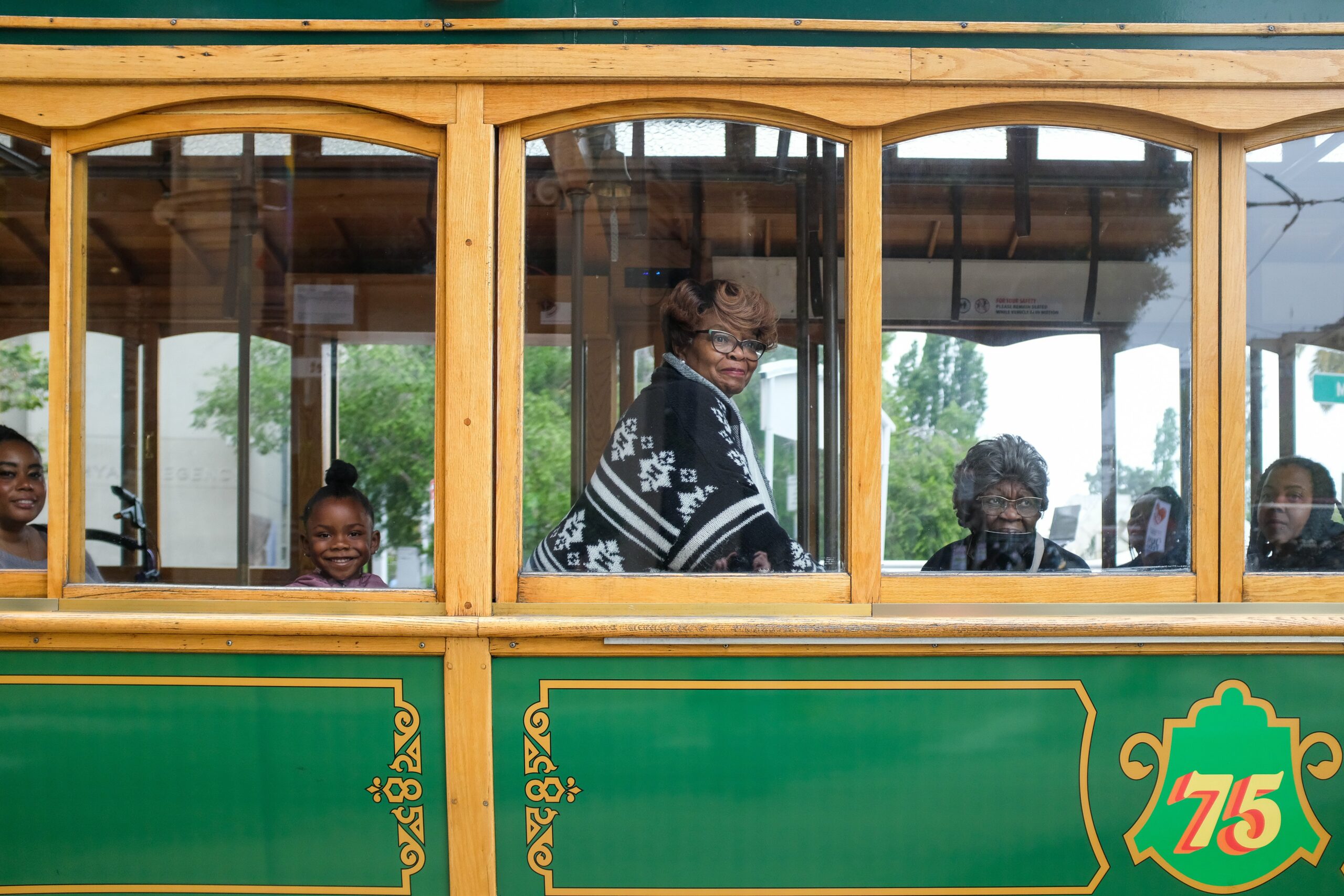 Passengers smile inside a vintage green and yellow trolley car.