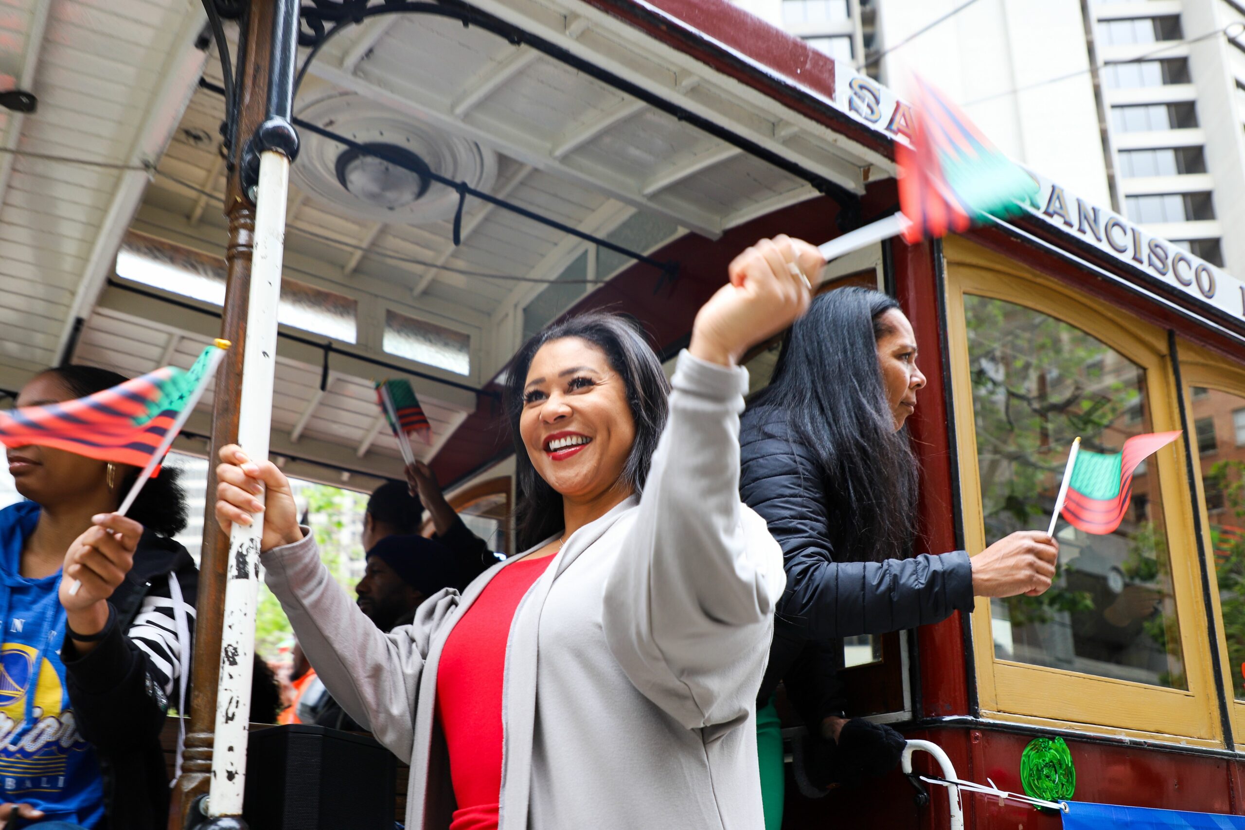 People are waving small flags joyfully on a San Francisco cable car.