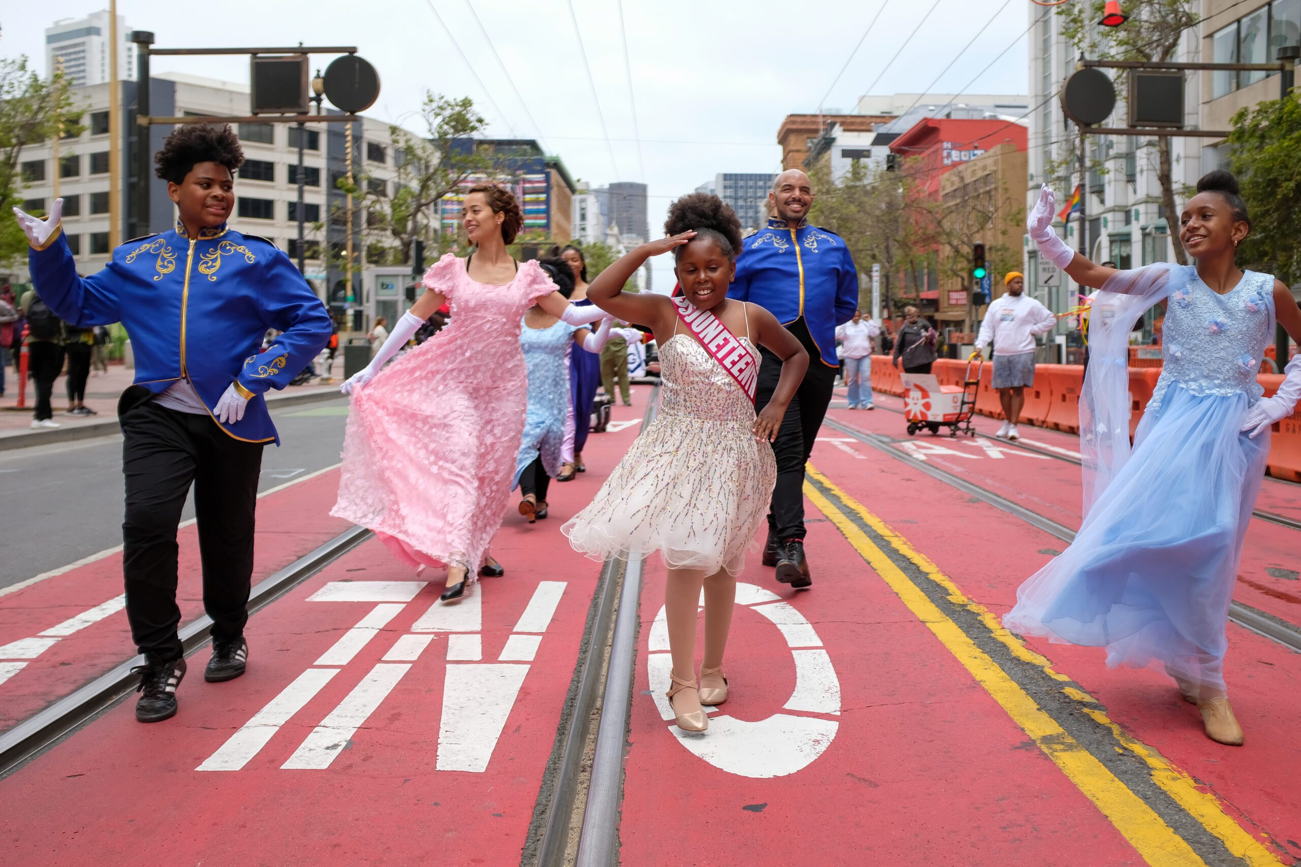 People in formal attire and costumes dancing joyfully on a red-painted street.