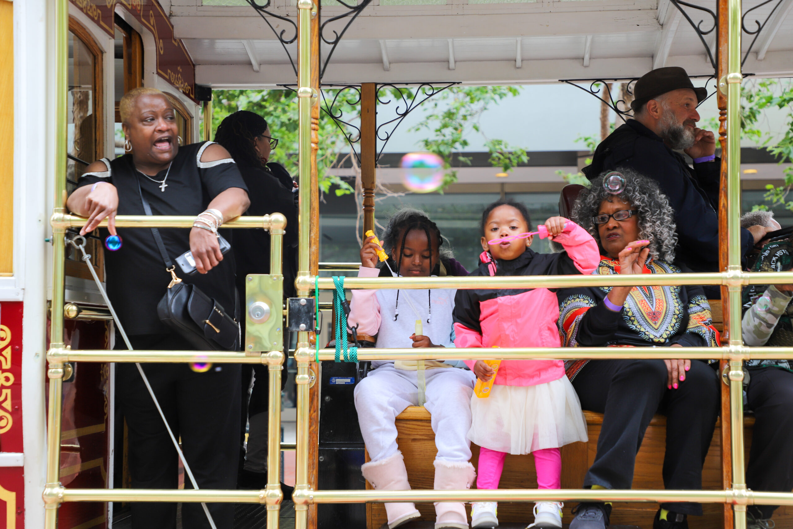People of various ages are riding a trolley, some blowing bubbles, with joyful expressions.