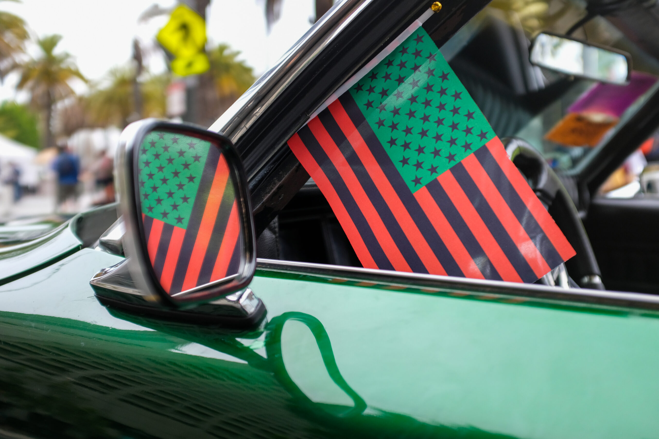 A car mirror reflects a U.S. flag with an alternative design featuring black and red stripes and a green starfield.