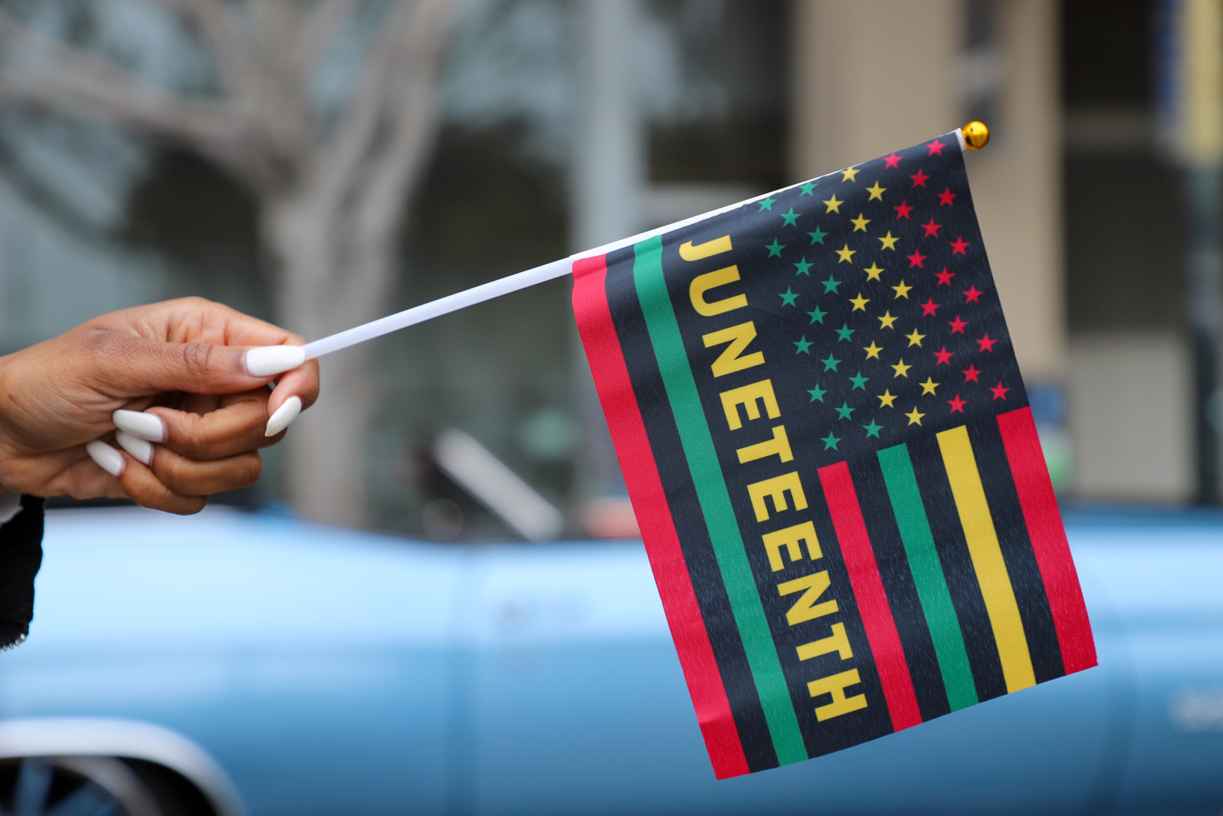 A hand holds a flag with &quot;JUNETEENTH&quot; and red, green, and yellow stripes &amp; stars.