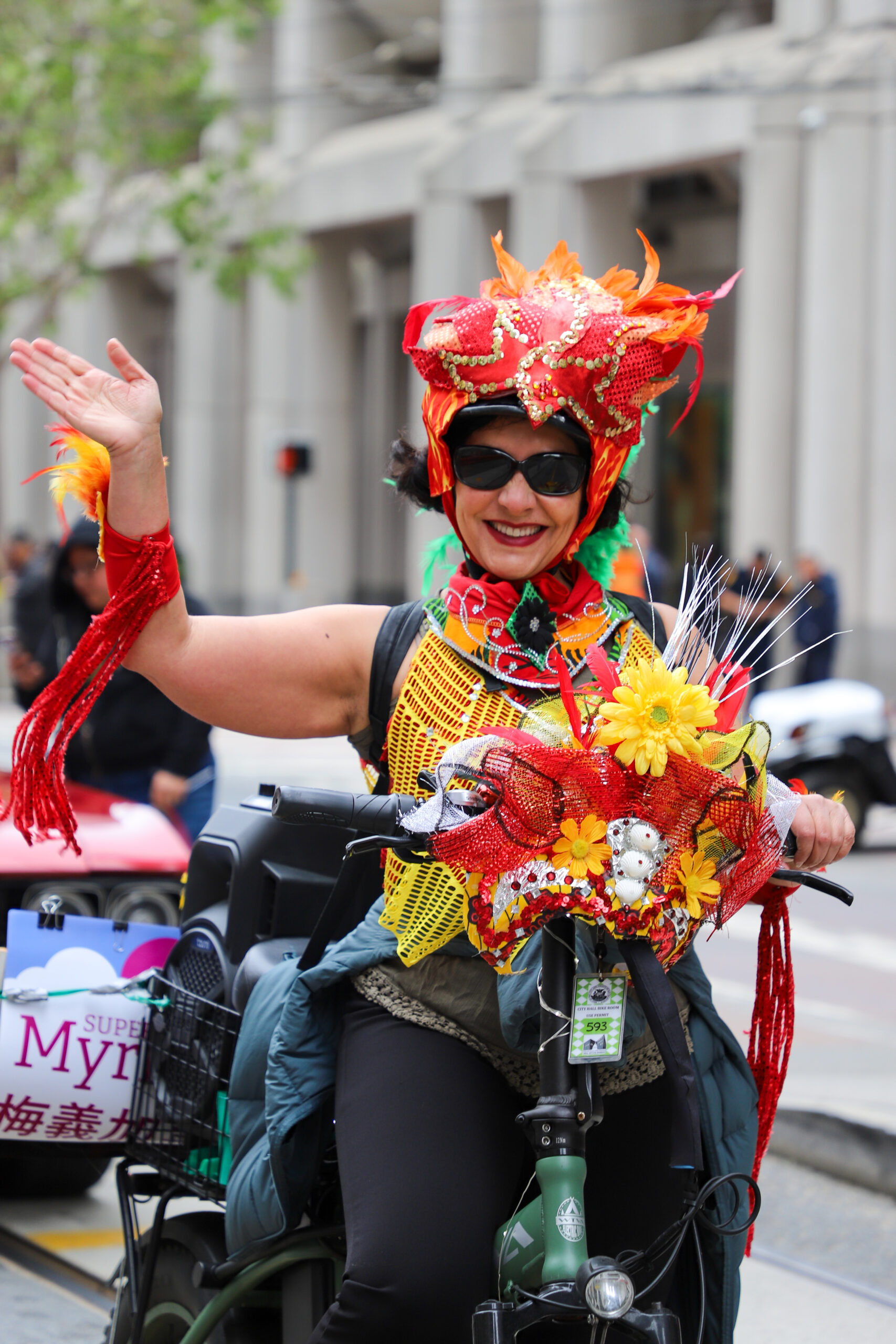 A person in a brightly colored costume rides a scooter, waving at the camera.