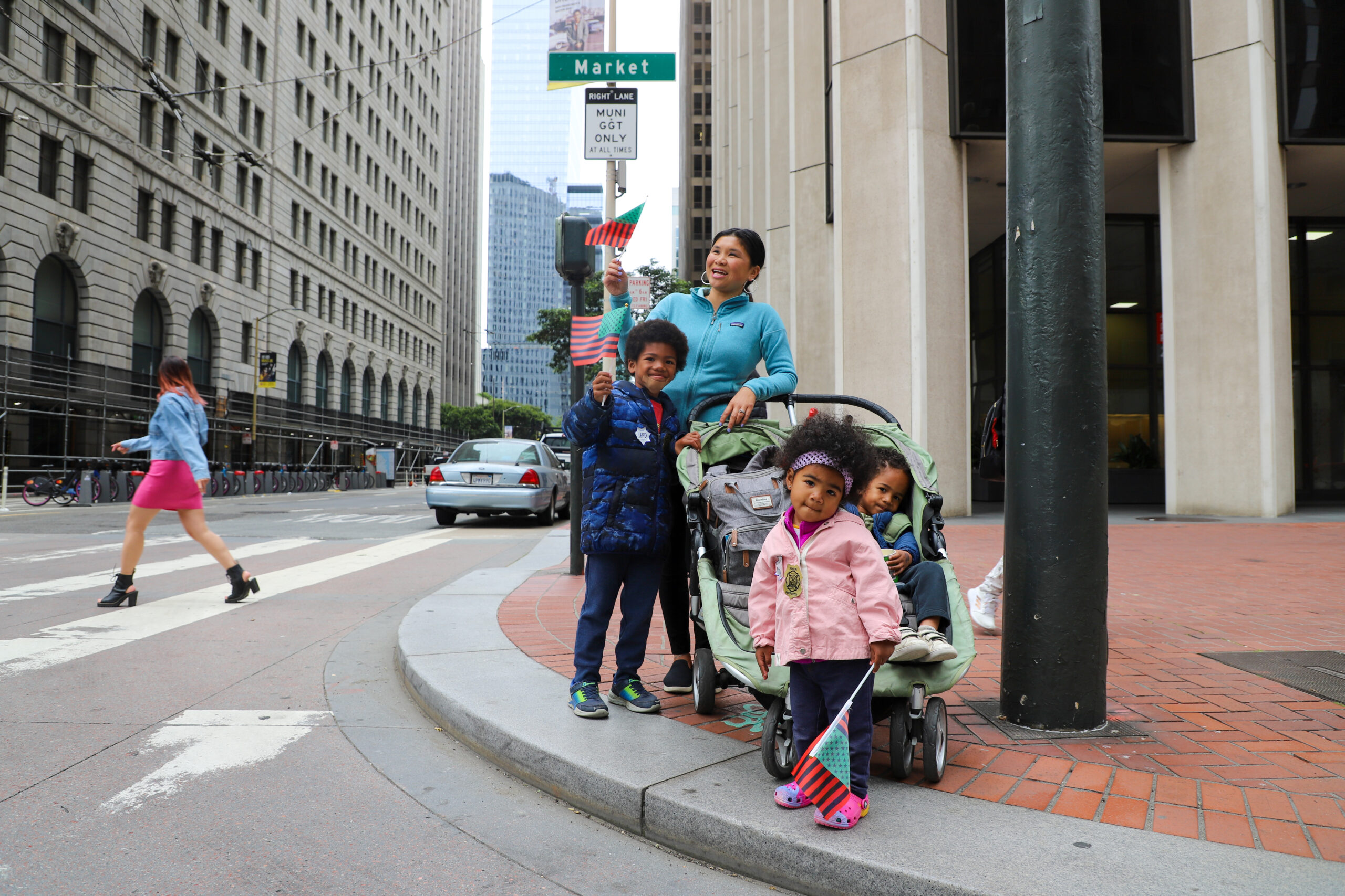 A woman and three kids on a sidewalk. One child is waving a flag.