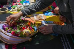 Hands selecting flowers from a basket on a colorful table. Crafting materials are visible.
