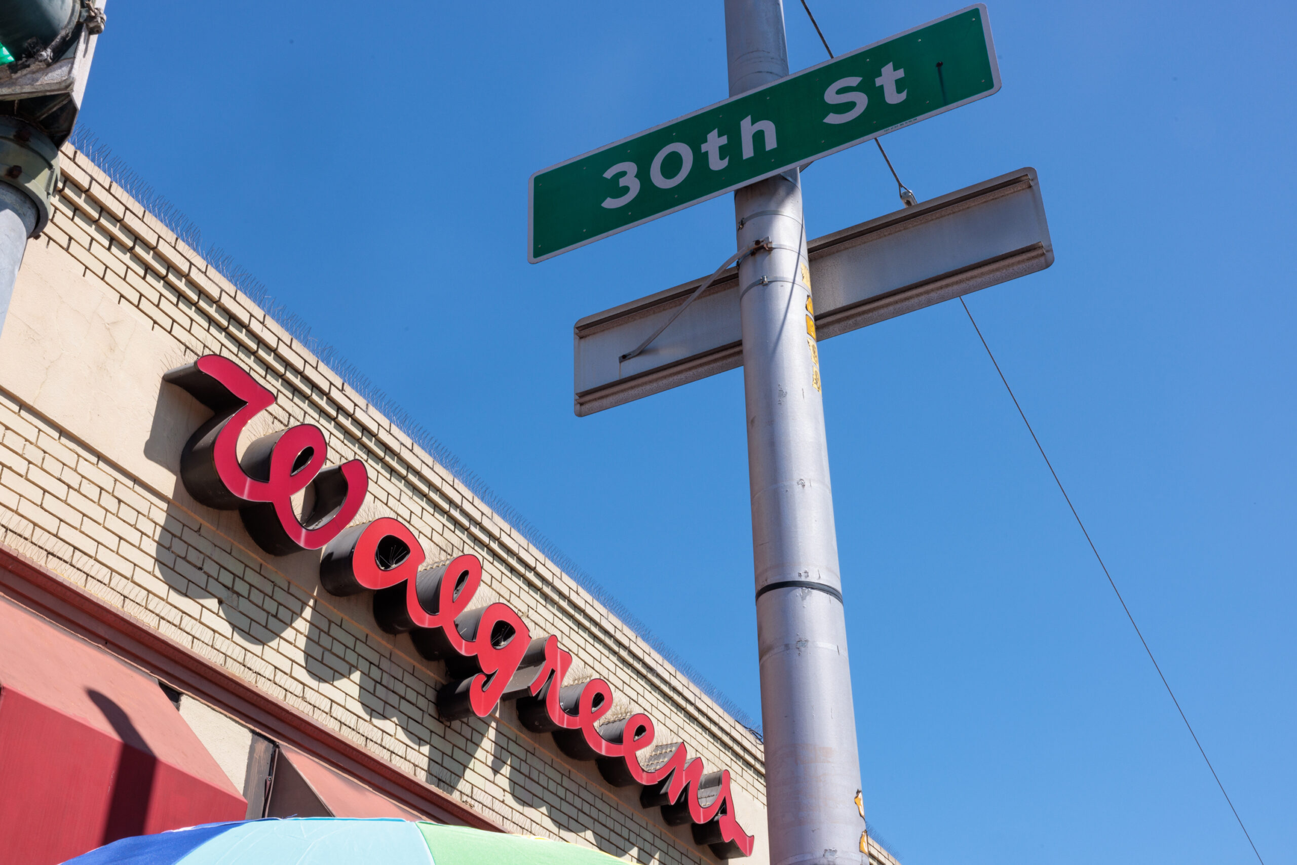 Street signs "30th St" and a Walgreens store with a red sign on a brick building, under a clear blue sky.