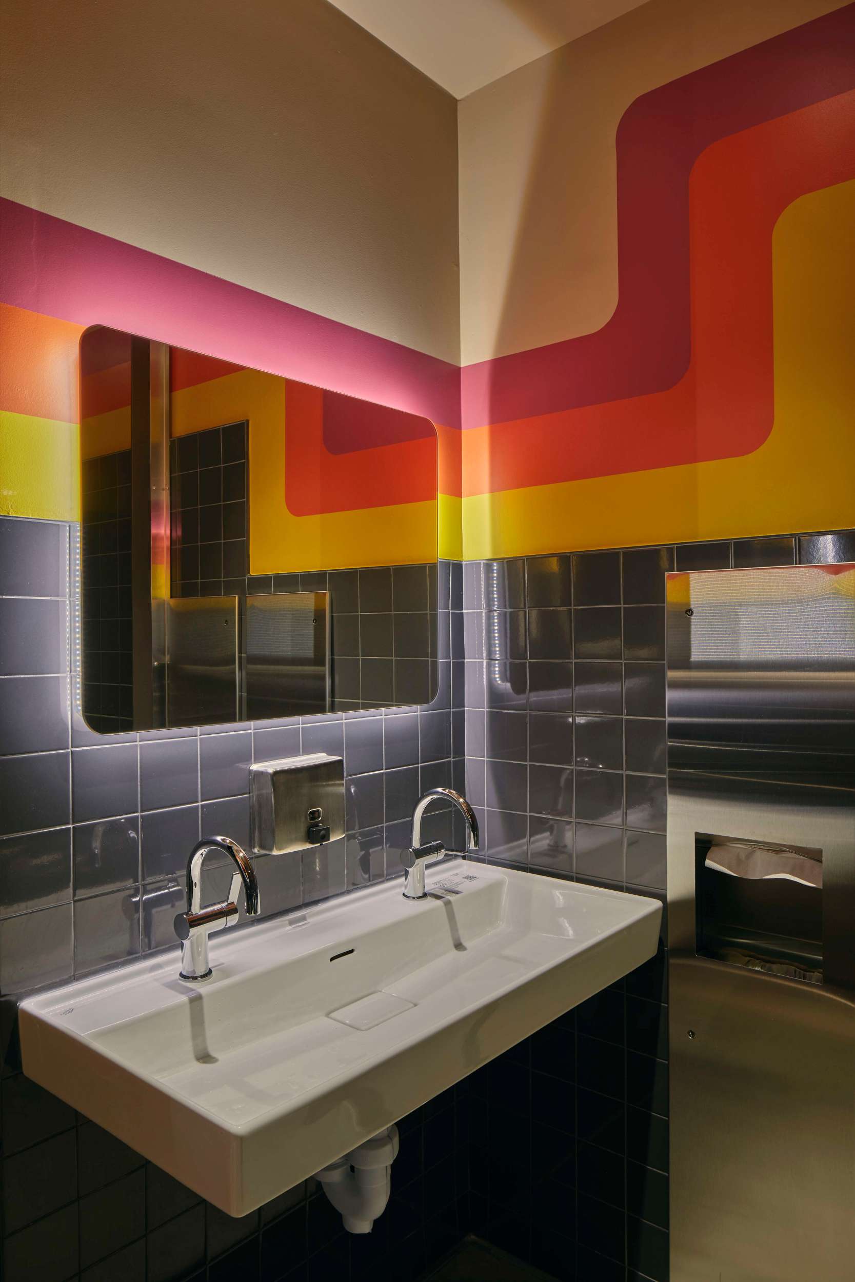 multi-colored bathroom including yellow, orange, and red stripes, with a sink and mirror pictured