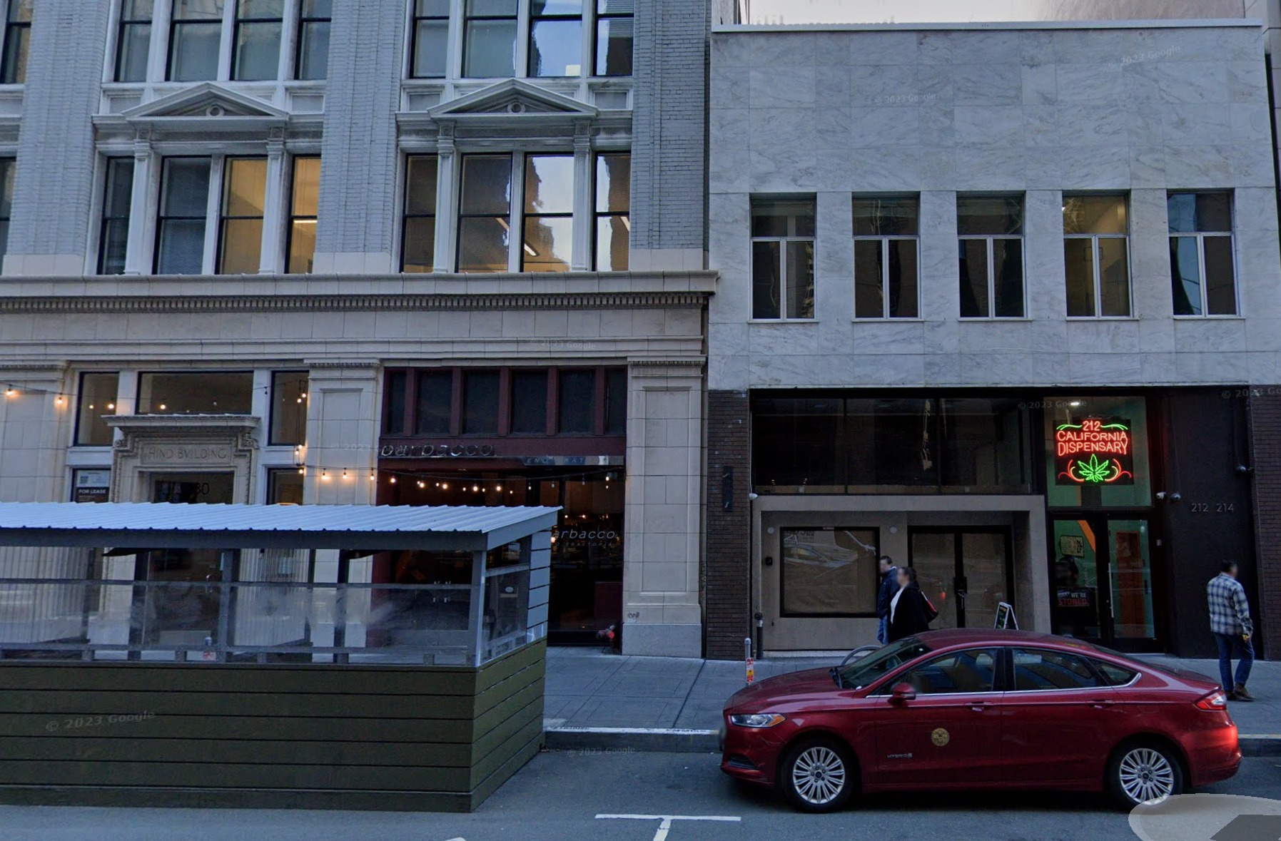 Urban street with two buildings, one with &quot;California Dispensary&quot; sign, a parked red car, and a few pedestrians.