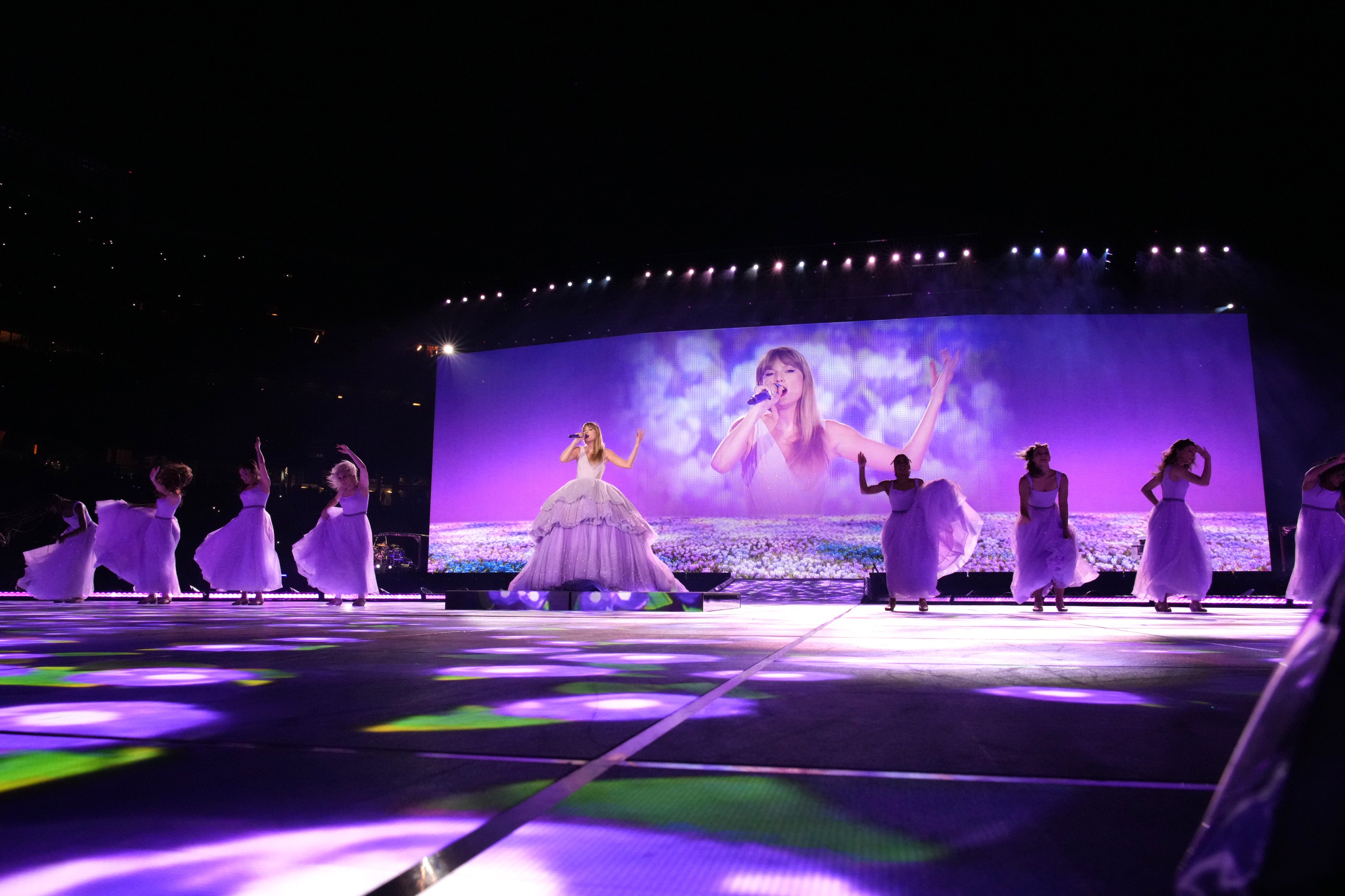 A singer on stage with dancers; a large screen showing the artist singing in a field.