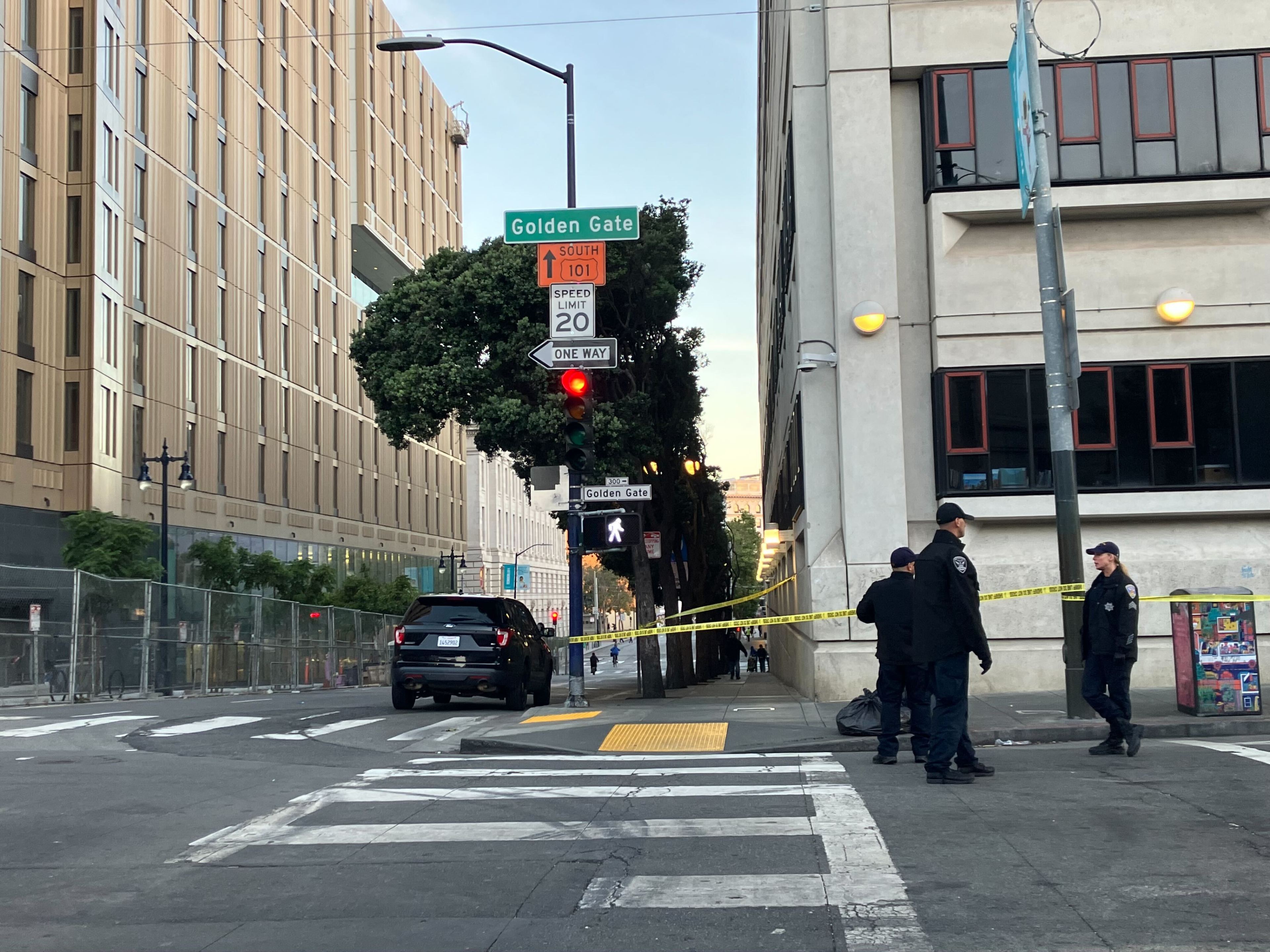 Urban street corner with police officers, a caution tape barrier, and a parked SUV. Street signs indicate "Golden Gate" and route "101 South."
