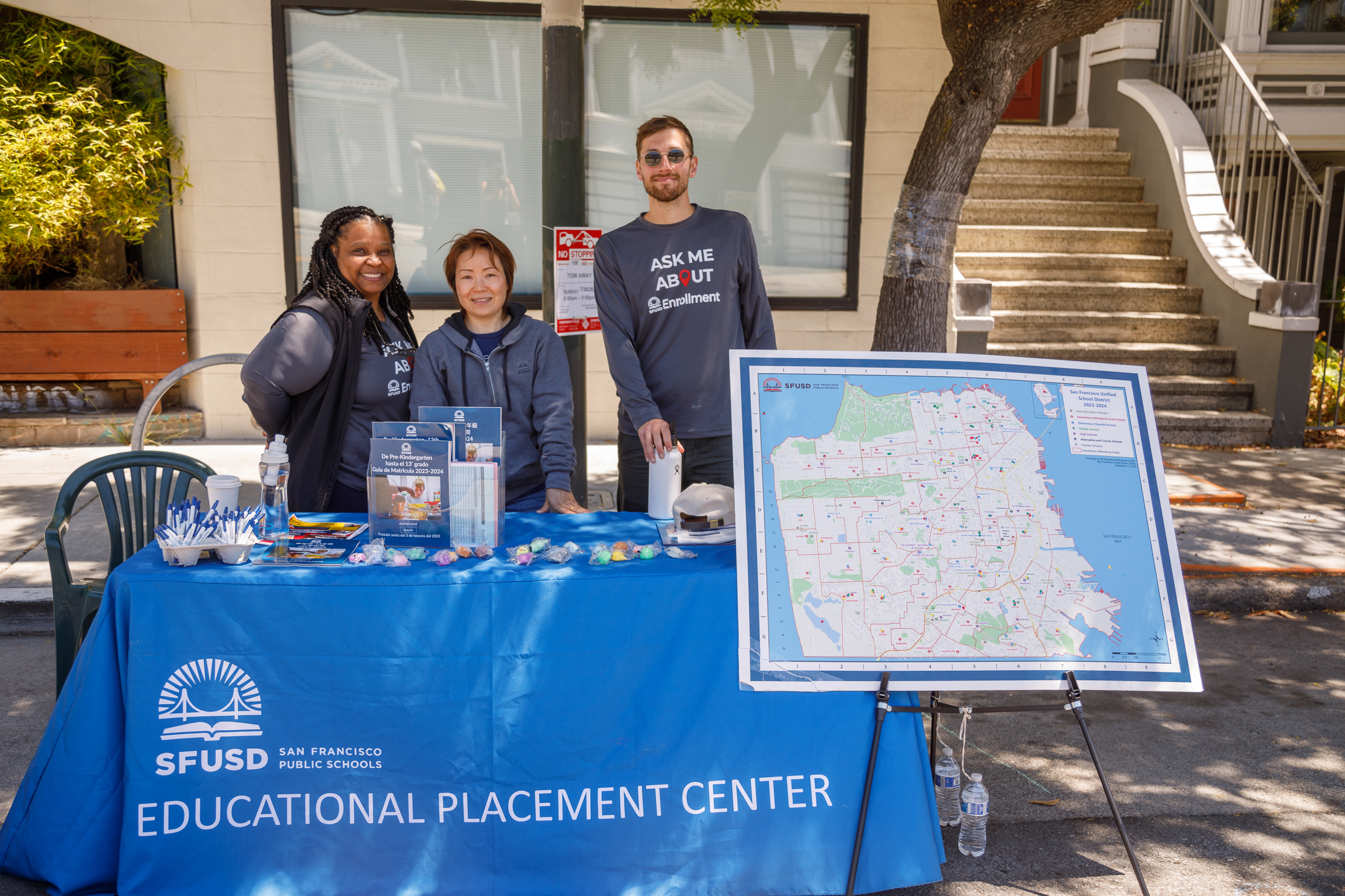 Three people stand behind a table from the SFUSD Educational Placement Center with informational materials and a map.