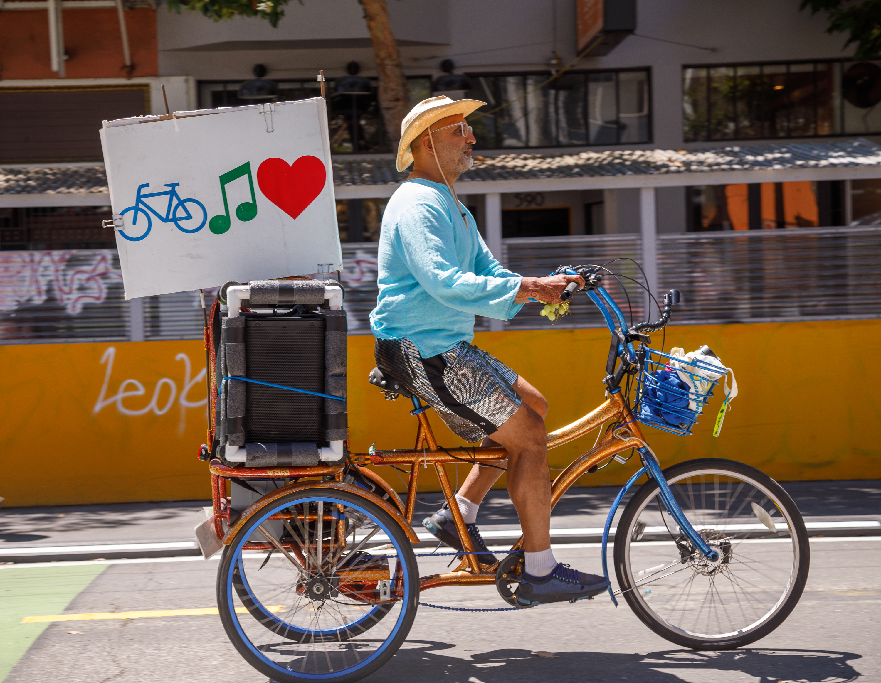 A man on a tricycle with a music speaker and a sign featuring a bike, musical note, and heart.