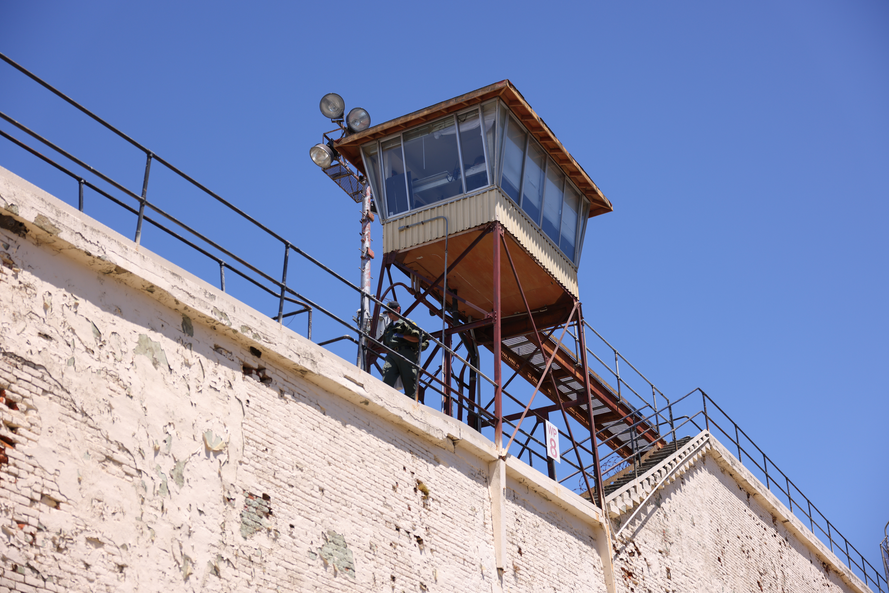 A weathered guard tower atop a high wall with stairs, against a clear blue sky.