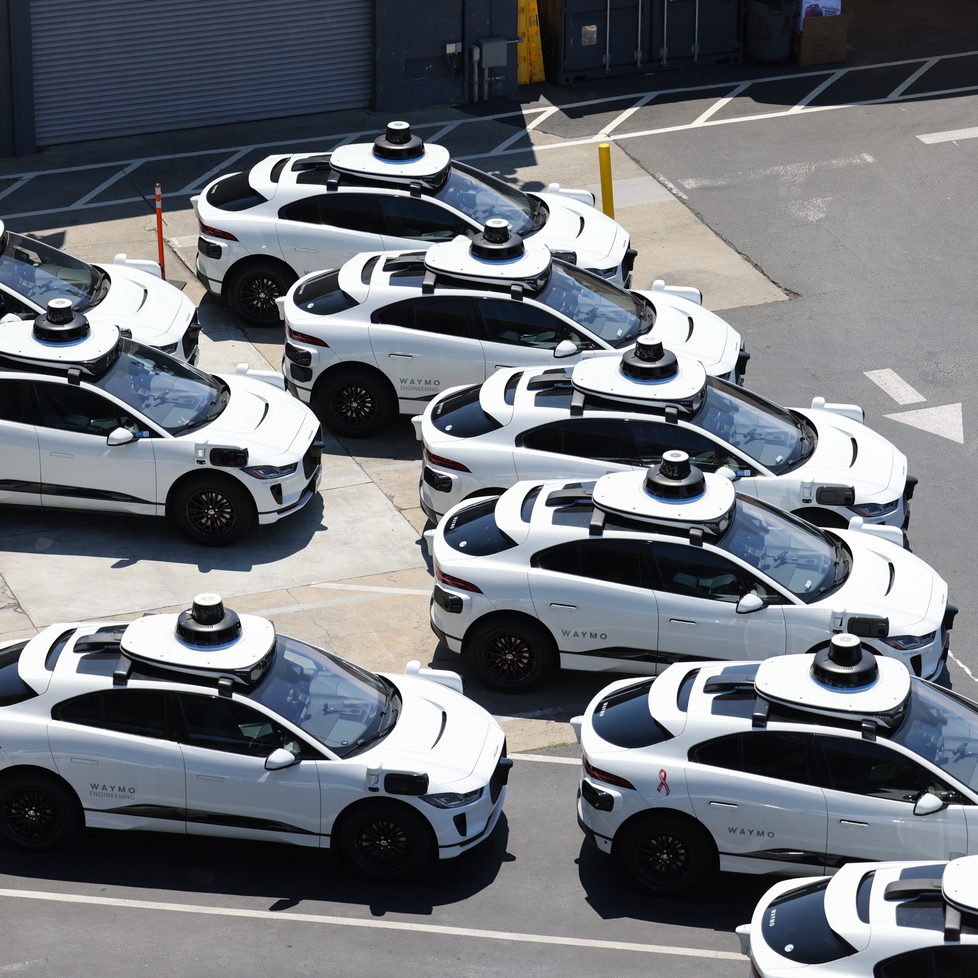 A group of white self-driving cars with rooftop sensors are parked closely together in a lot, ready for use or testing.