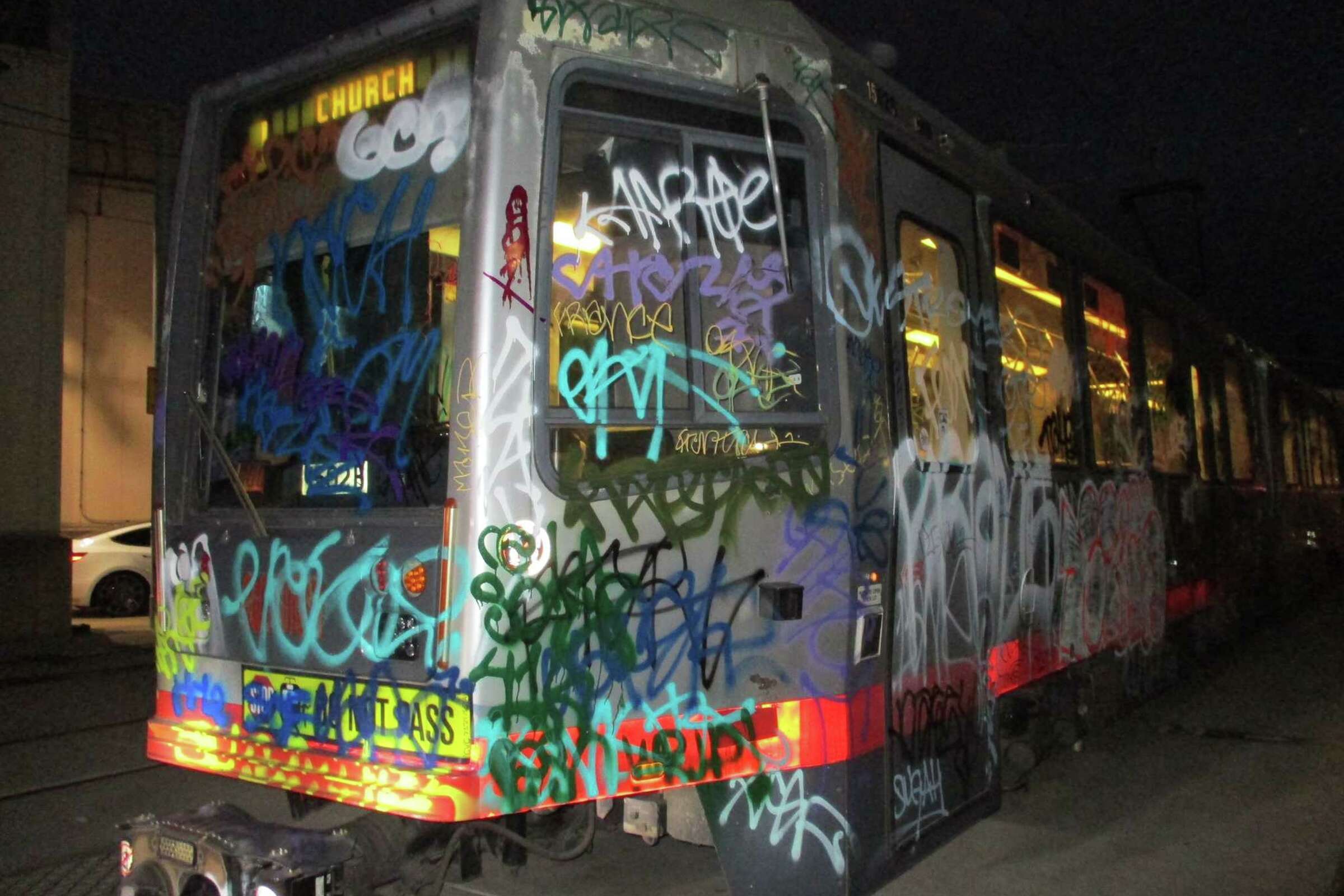 A graffiti-covered tram at night, with colorful tags and scribbles obscuring its windows and surface.
