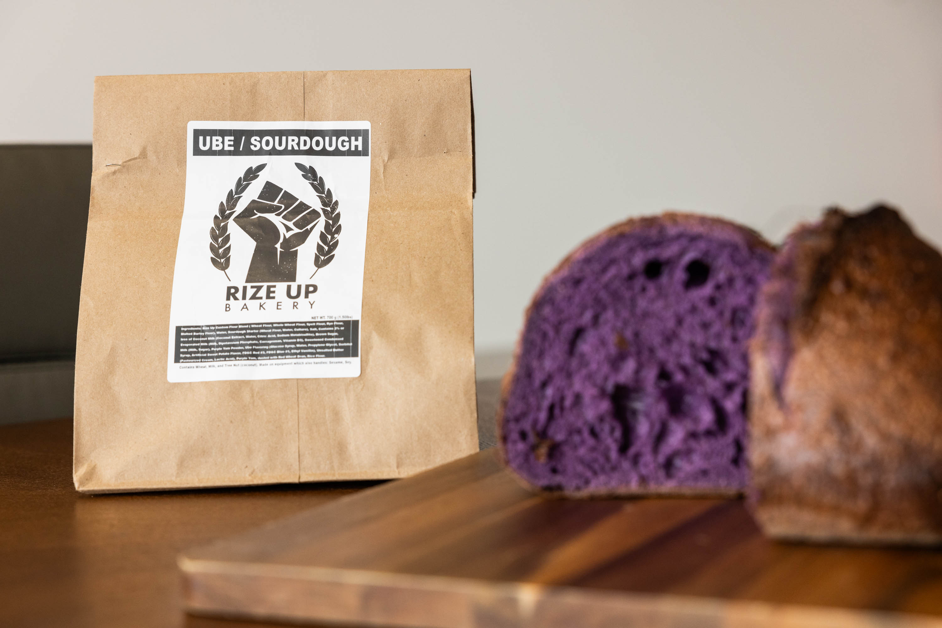 a brown paper bag is seen next to a loaf of bread that has been sliced open revealing purple dough inside