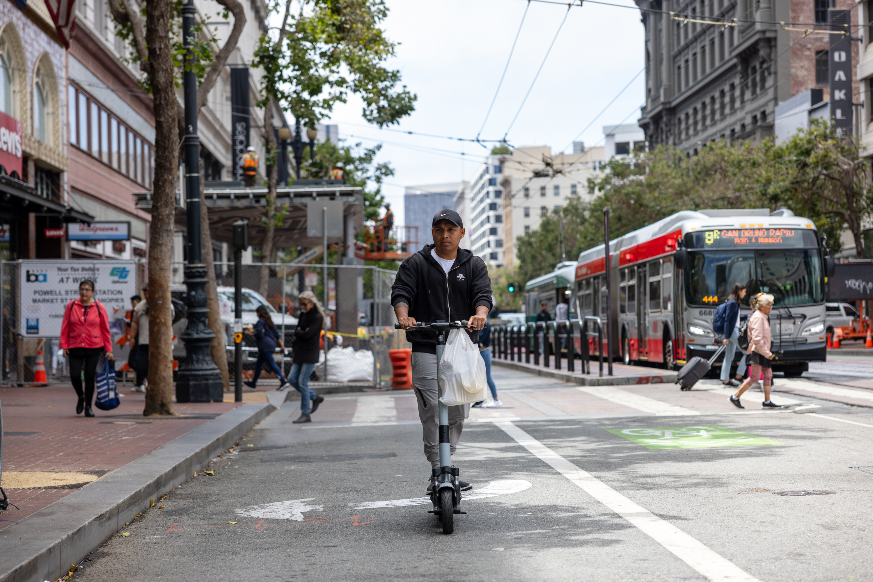 A person on a scooter on Market Street with a bus and pedestrians in the background.