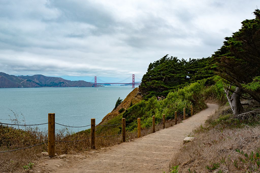 A scene of a trail above the ocean with the Golden Gate Bridge in the background.
