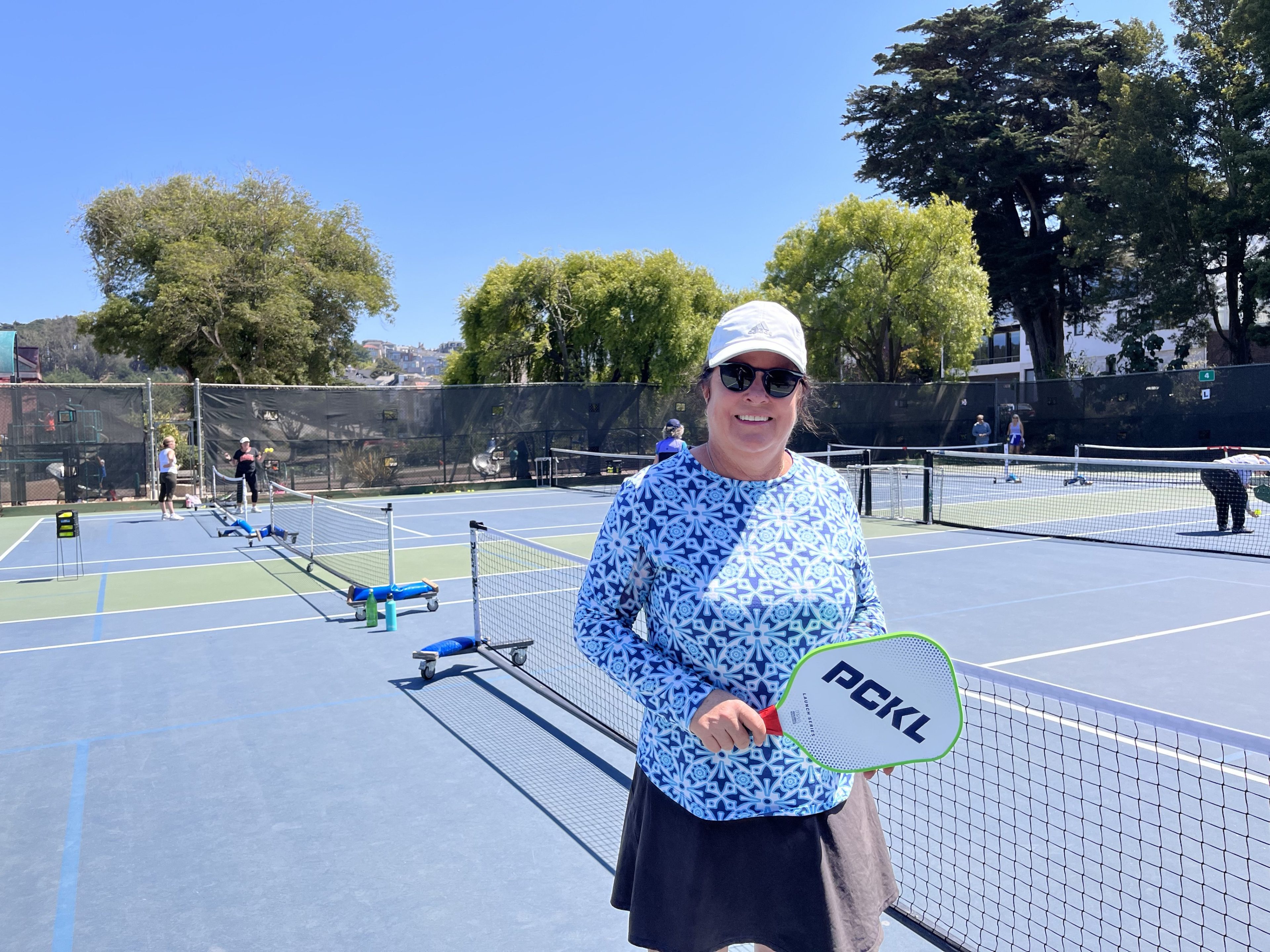 A woman stands with pickleball paddle in front of a net and blue pickleball court at Presidio Wall Playground in San Francisco.