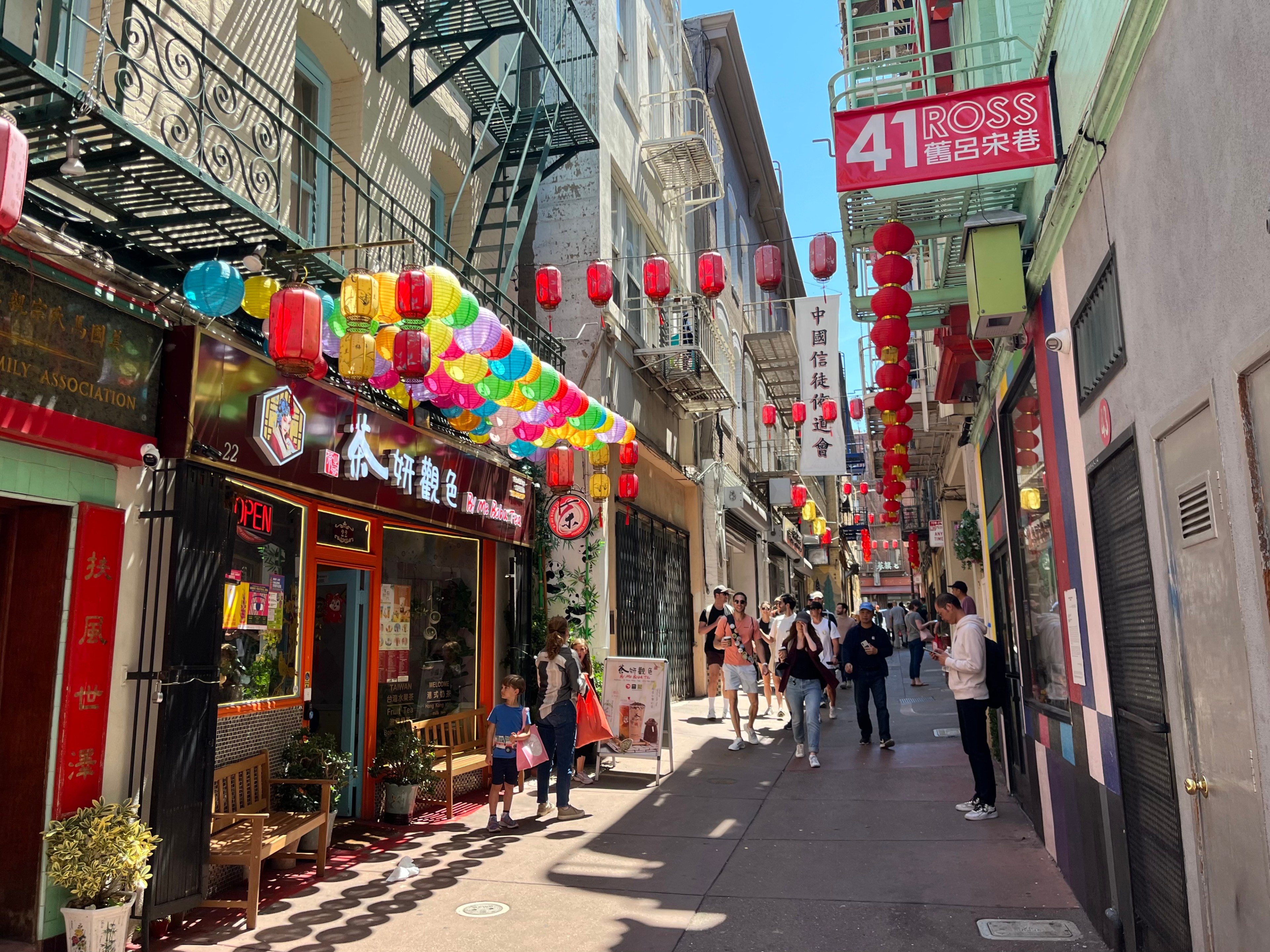 Colorful lanterns hang in a narrow San Francisco alleyway that has a red terrace and a red sign.