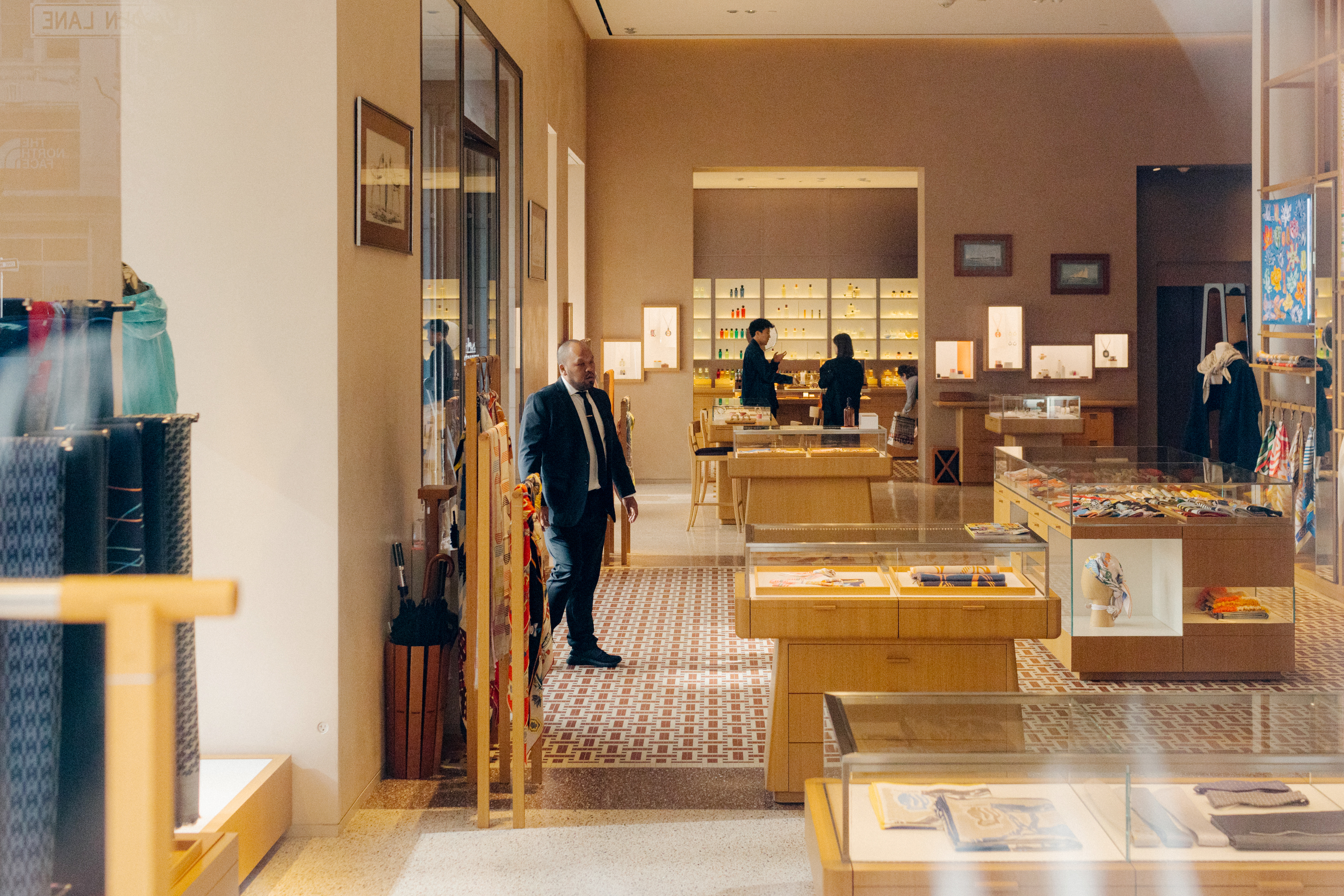 A man in a suit walks through a high-end boutique with displays of luxury goods and attentive staff.
