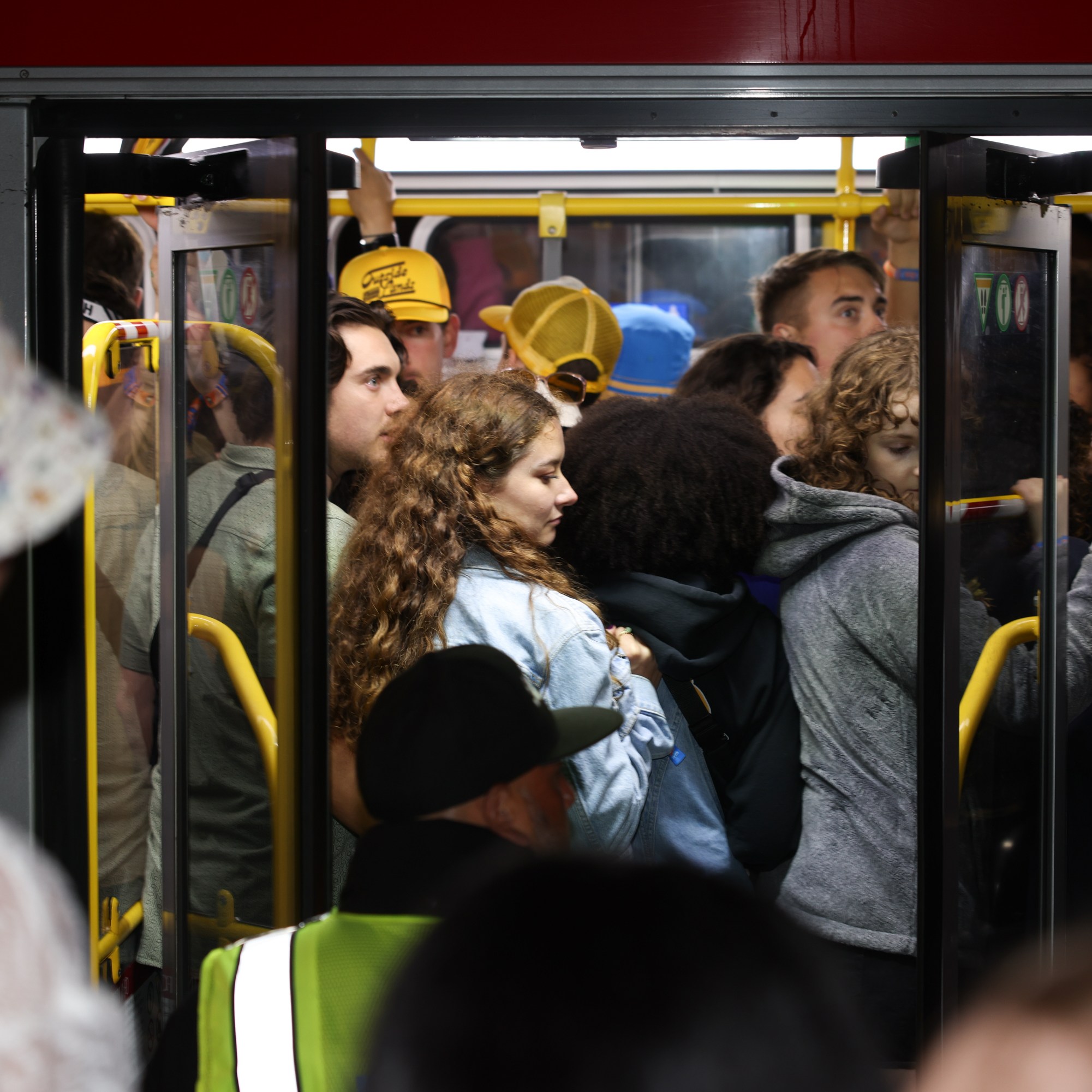 The image shows a crowded bus with many people tightly packed near its doors, some wearing jackets and hats, and others standing close together inside the vehicle.