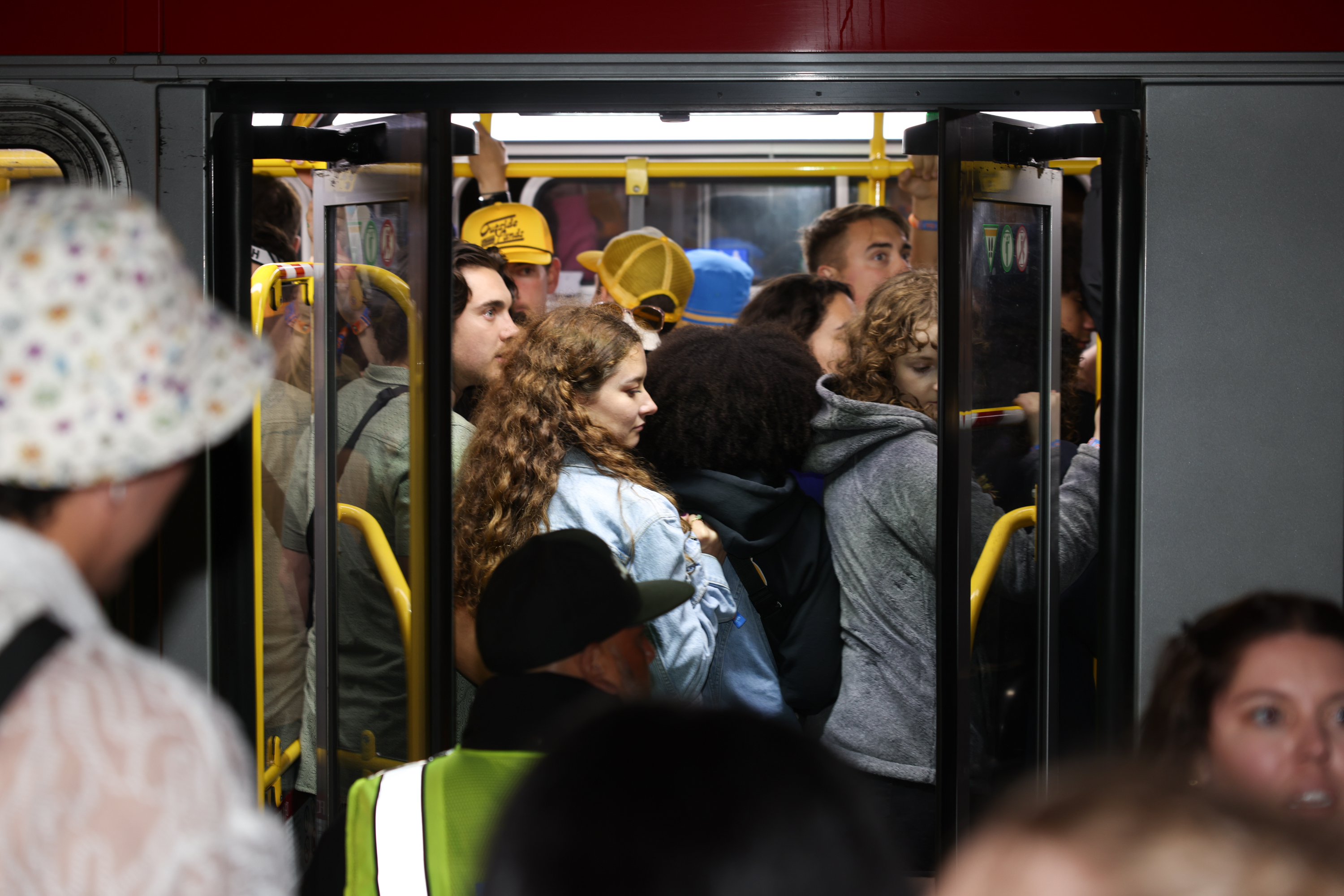 The image shows a crowded bus with many people tightly packed near its doors, some wearing jackets and hats, and others standing close together inside the vehicle.