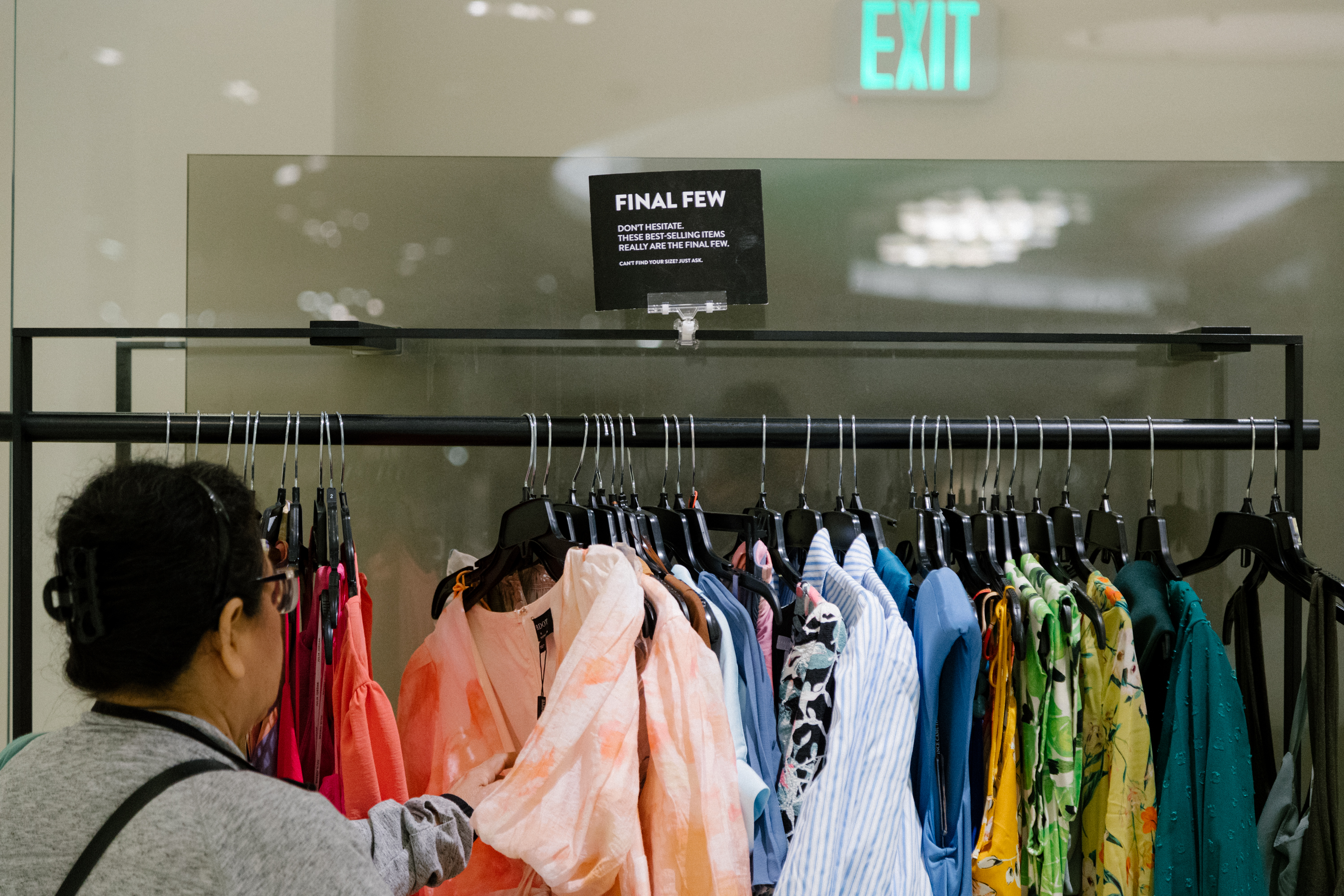 a woman shops at a clothing rack with brightly colored dresses