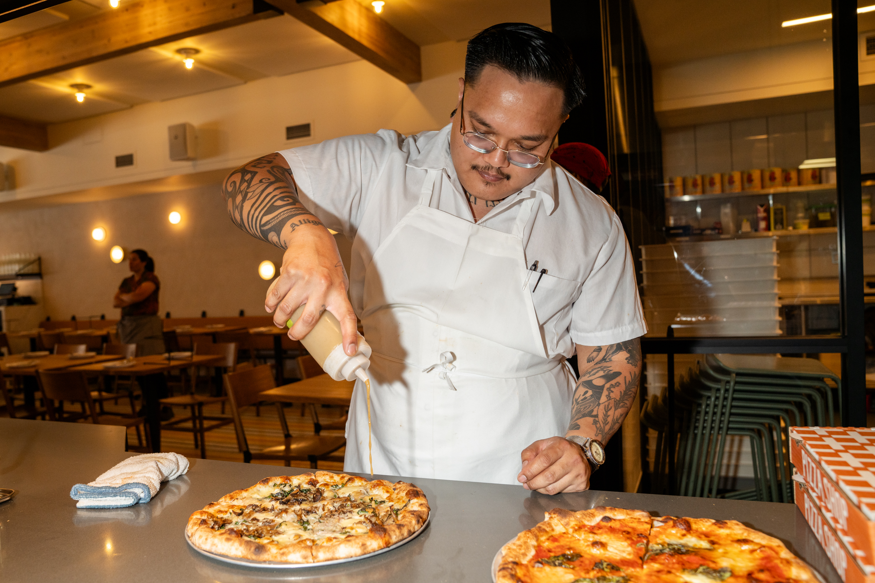 Sous Chef Mikee Tocus adds the finishing touches to freshly made pizzas at Flour + Water Pizzeria on Aug. 10, 2023.