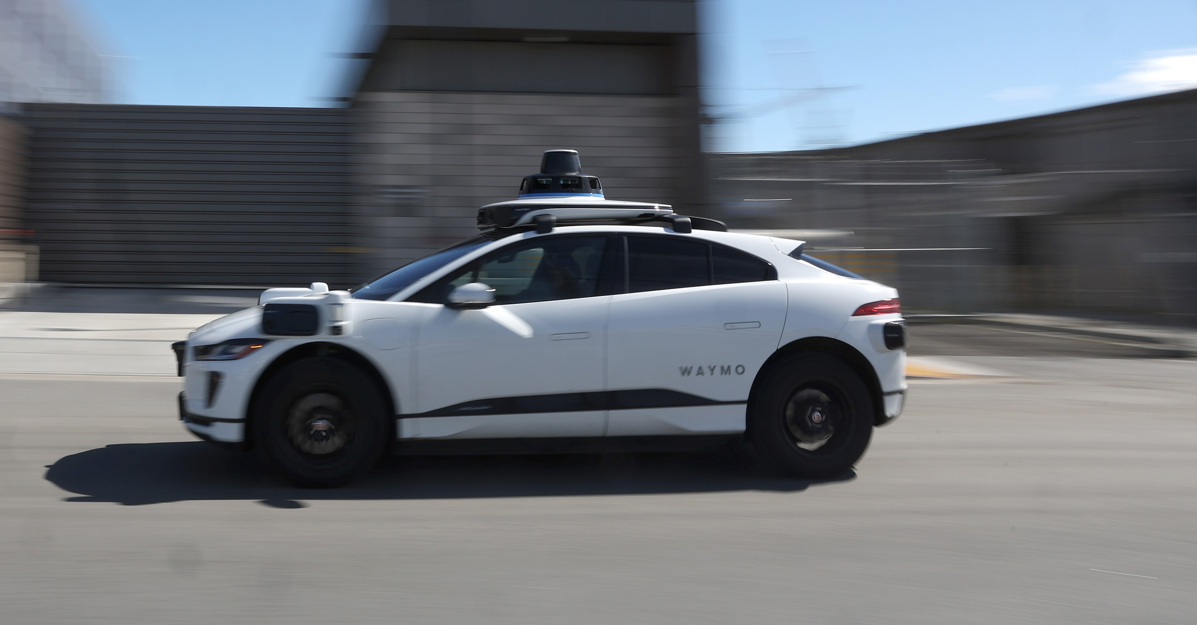 A white Waymo driverless SUV zips along a city street