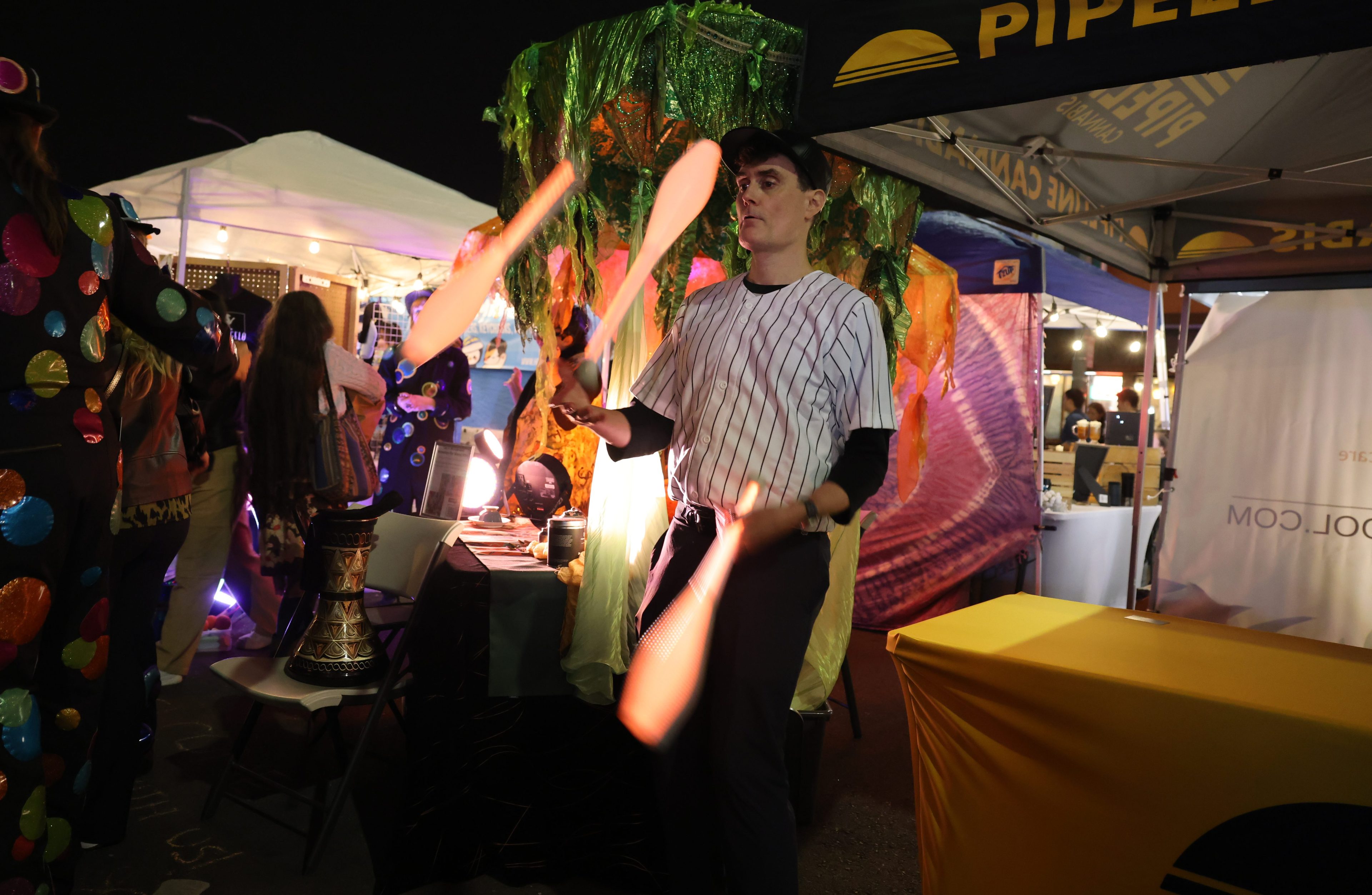 A person juggles clubs at a vibrant outdoor market with colorful tents and festive attire.