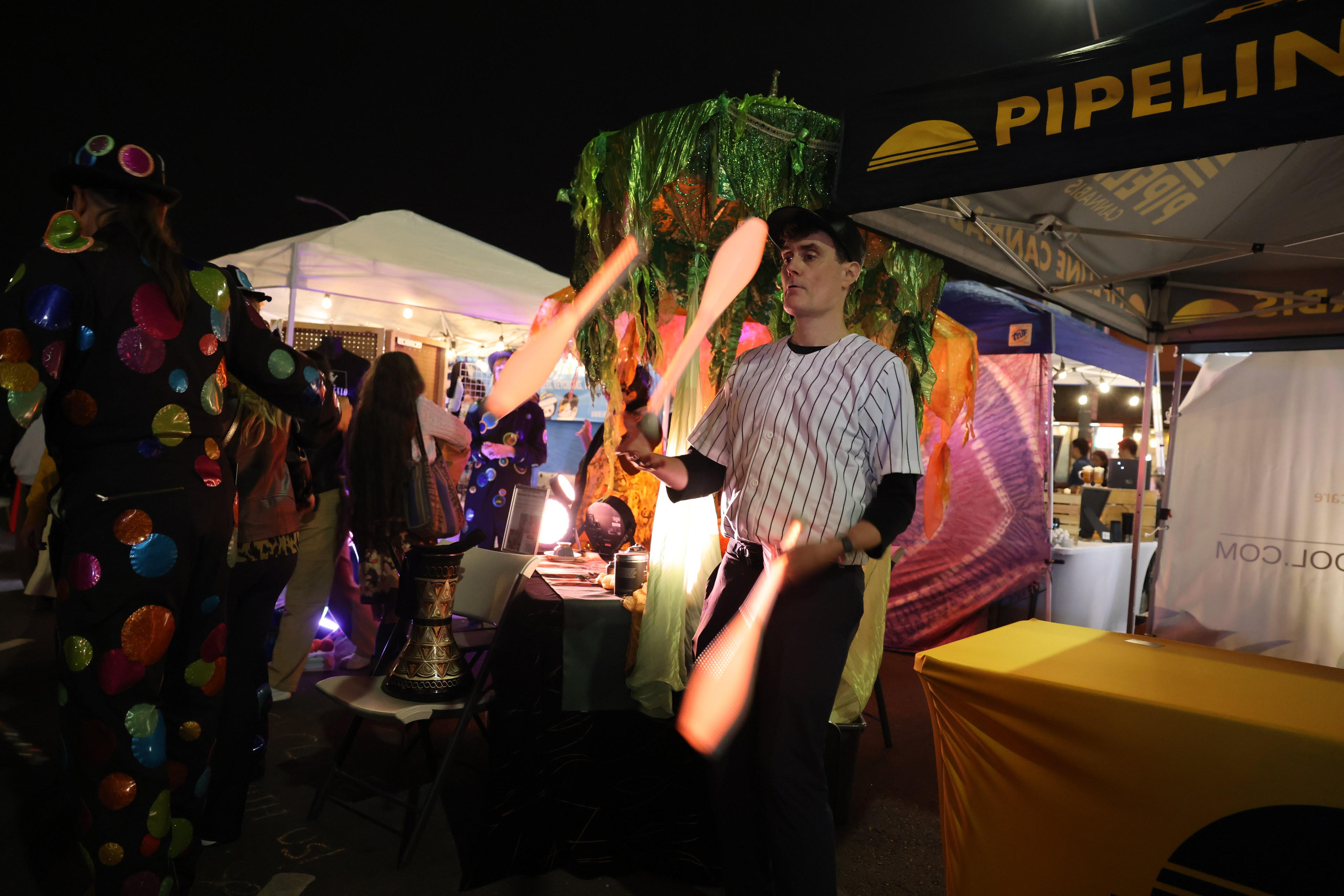 A person juggles clubs at a vibrant outdoor market with colorful tents and festive attire.