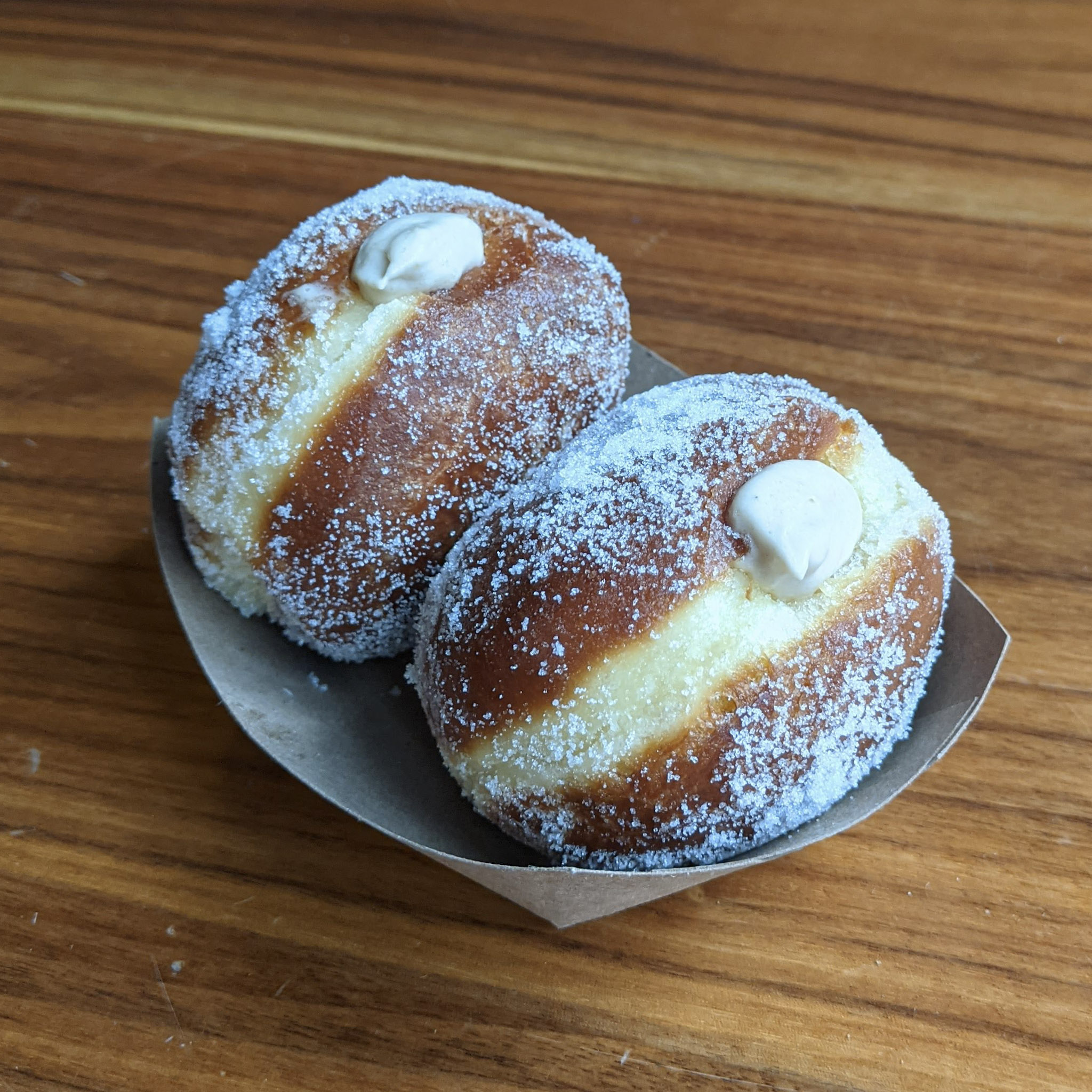 Two sugar-dusted donuts rest in a white cardboard bowl with pats of homemade butter melting atop them.