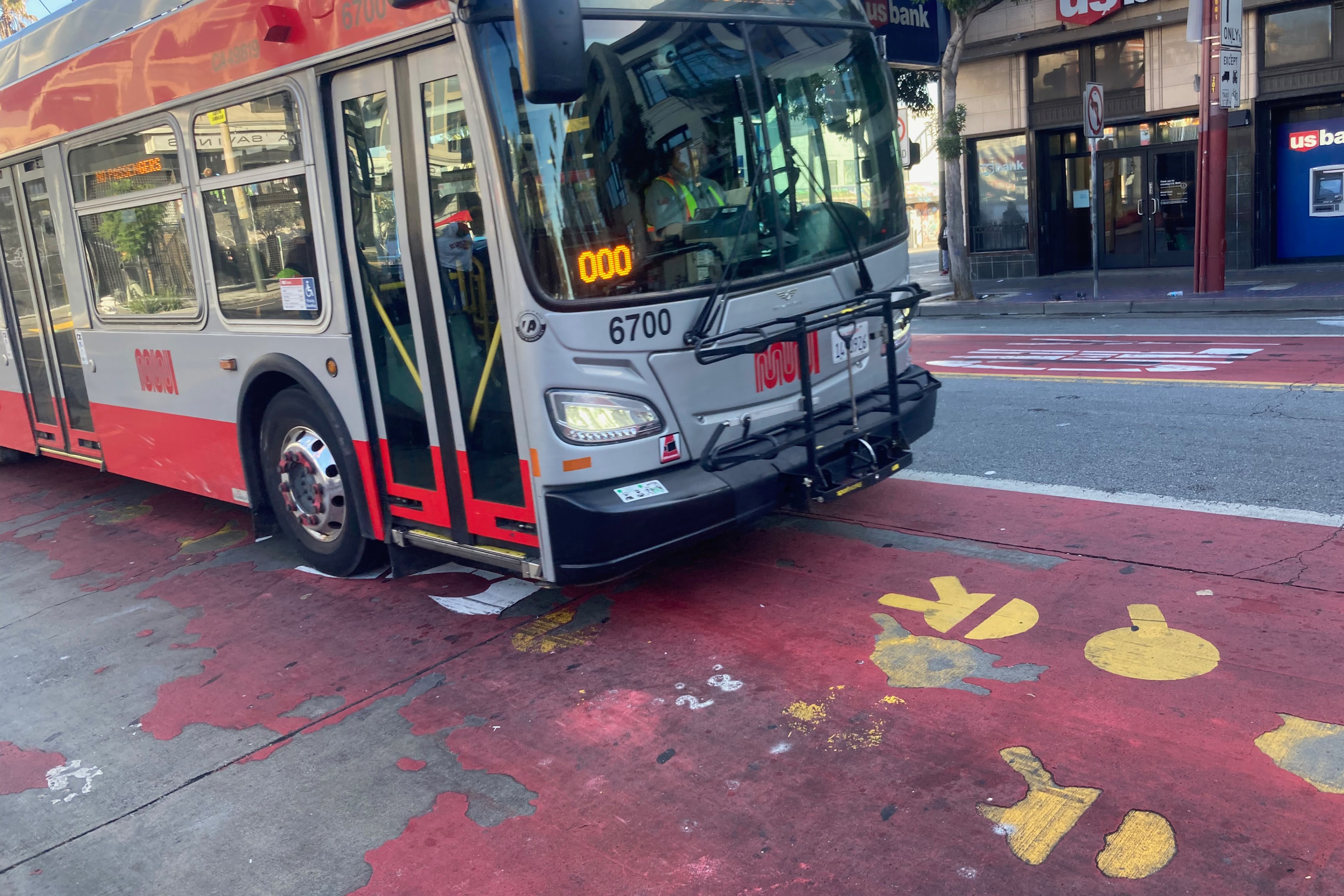 A red and white city bus is turning at an intersection with painted yellow footsteps on the pavement.