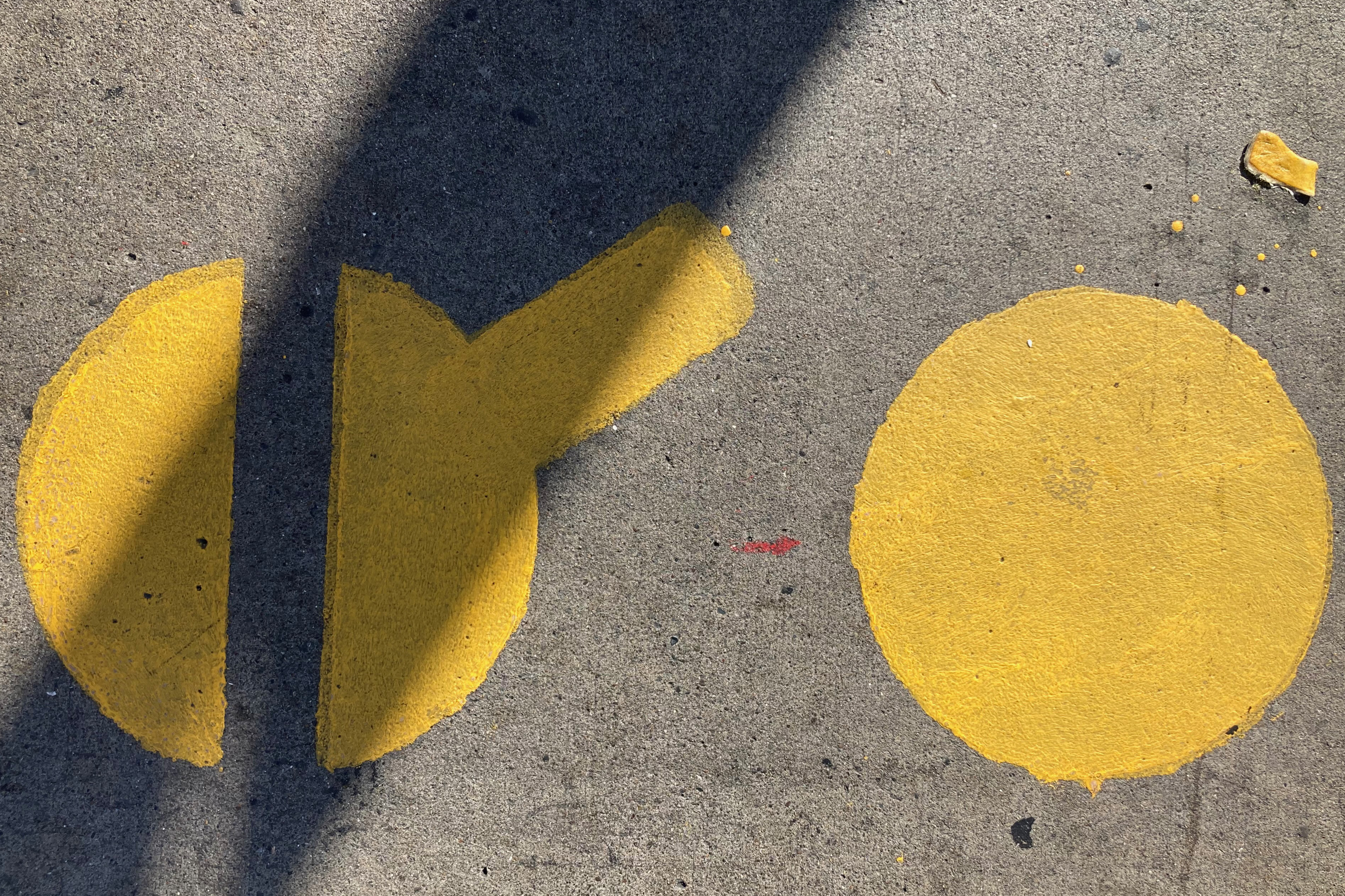 Yellow shapes on pavement with a shadow intersecting one, and a small orange peel nearby.