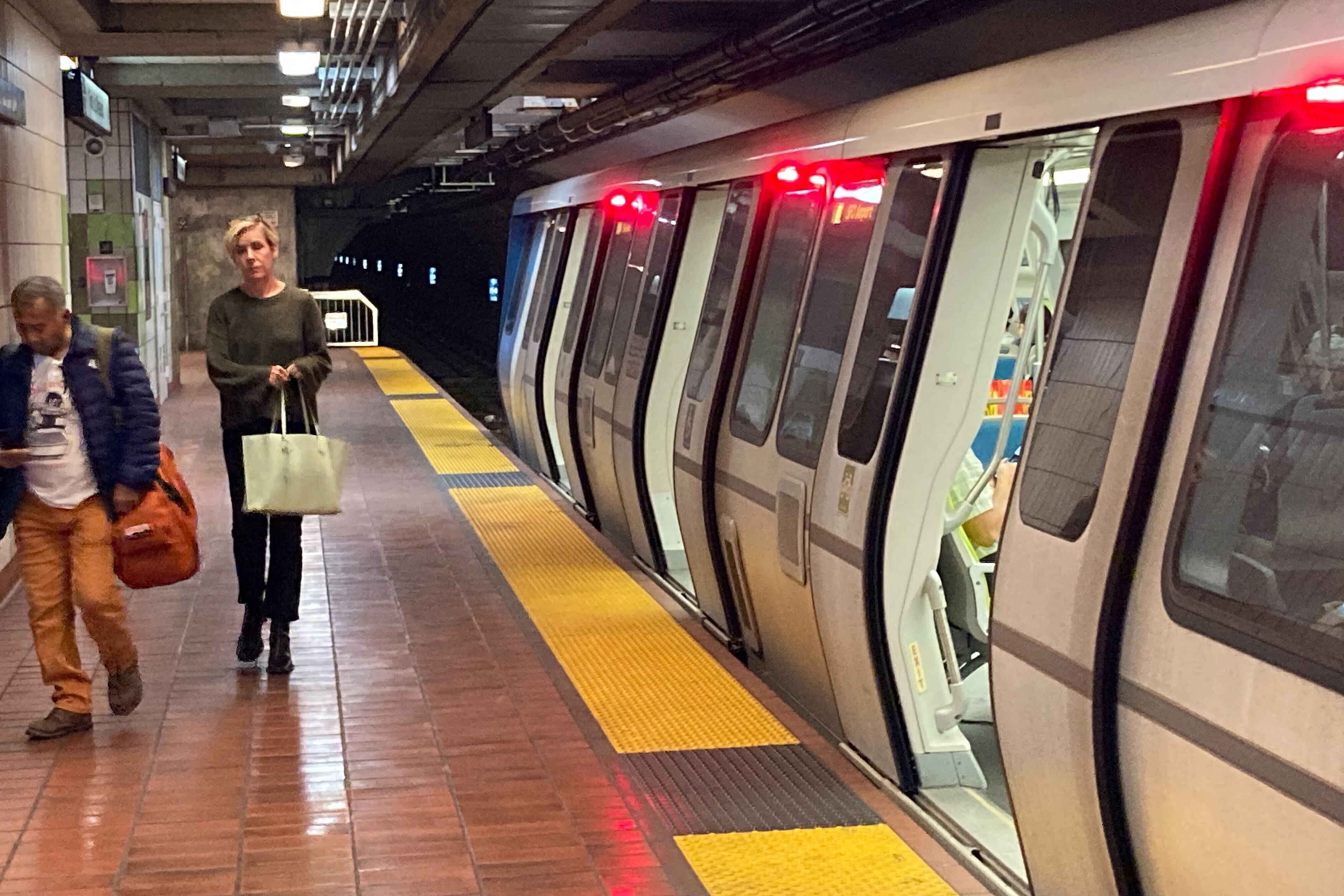 Passengers walk on a platform next to a train in an underground station.