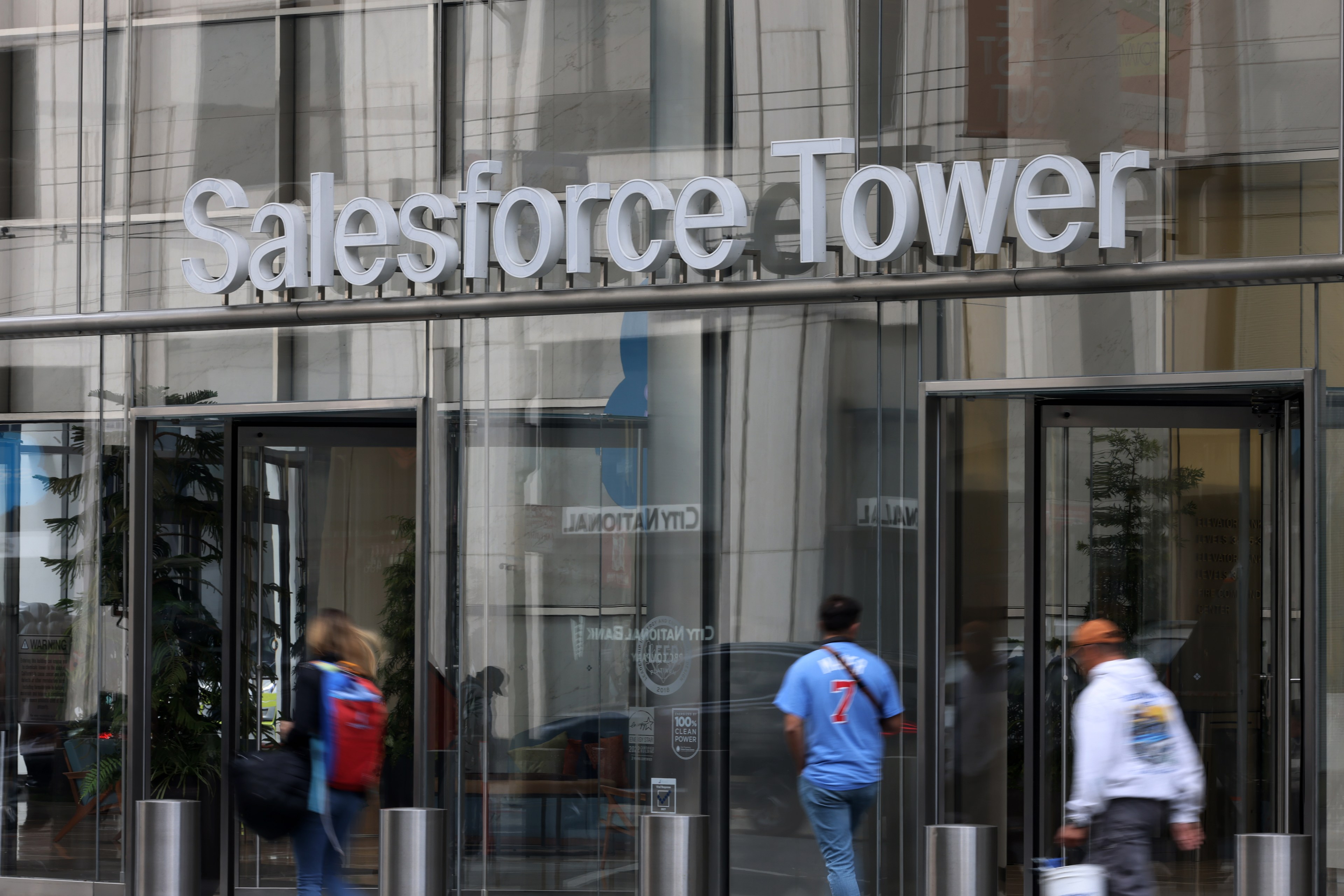 Sign "Salesforce Tower" above building entrance with people walking by.