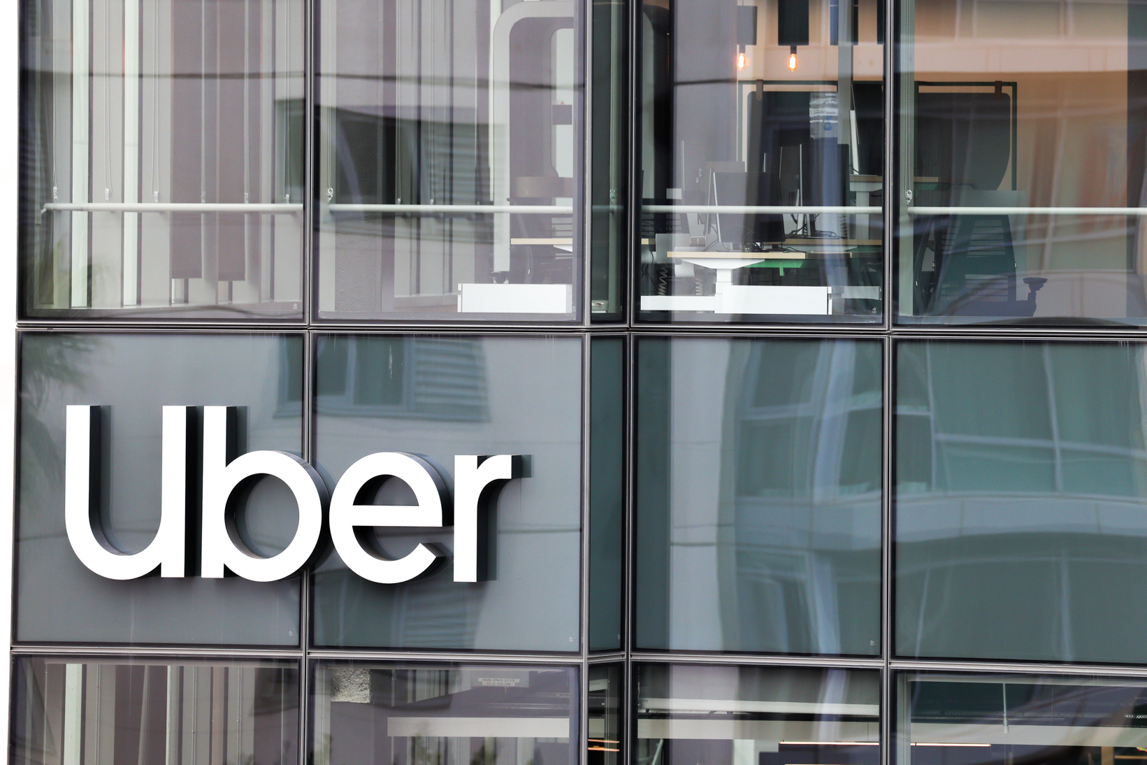 The image shows the large &quot;Uber&quot; logo on the exterior of a modern building with glass facade and reflections.