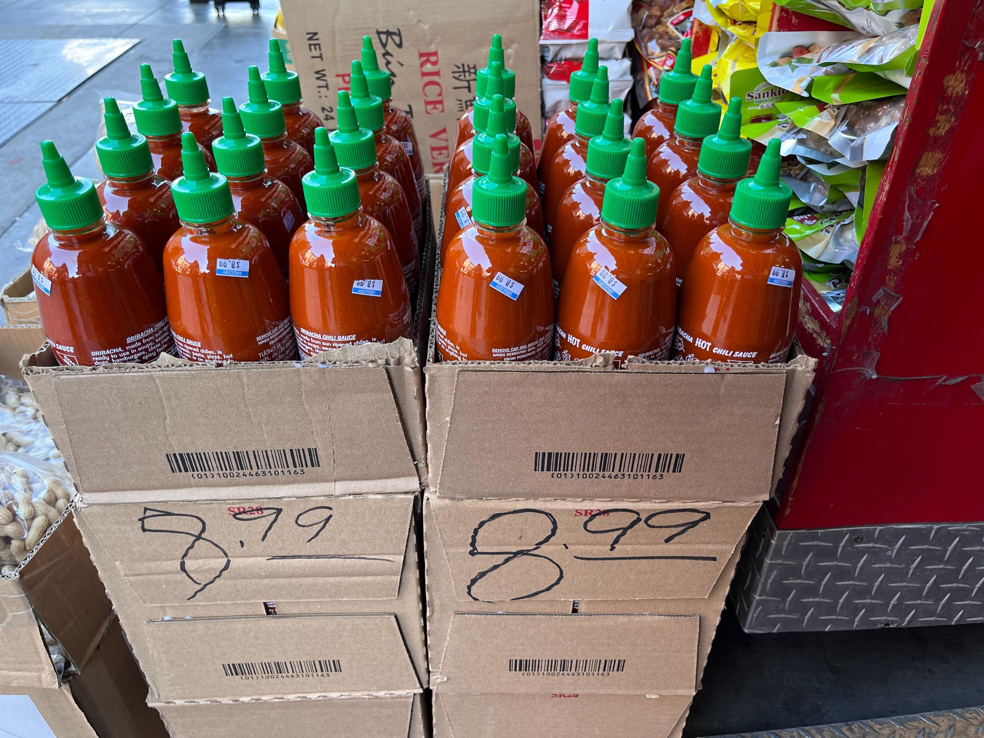 Bottles of hot chili sauce in boxes labeled with prices $7.99 and $8.99, displayed for sale.