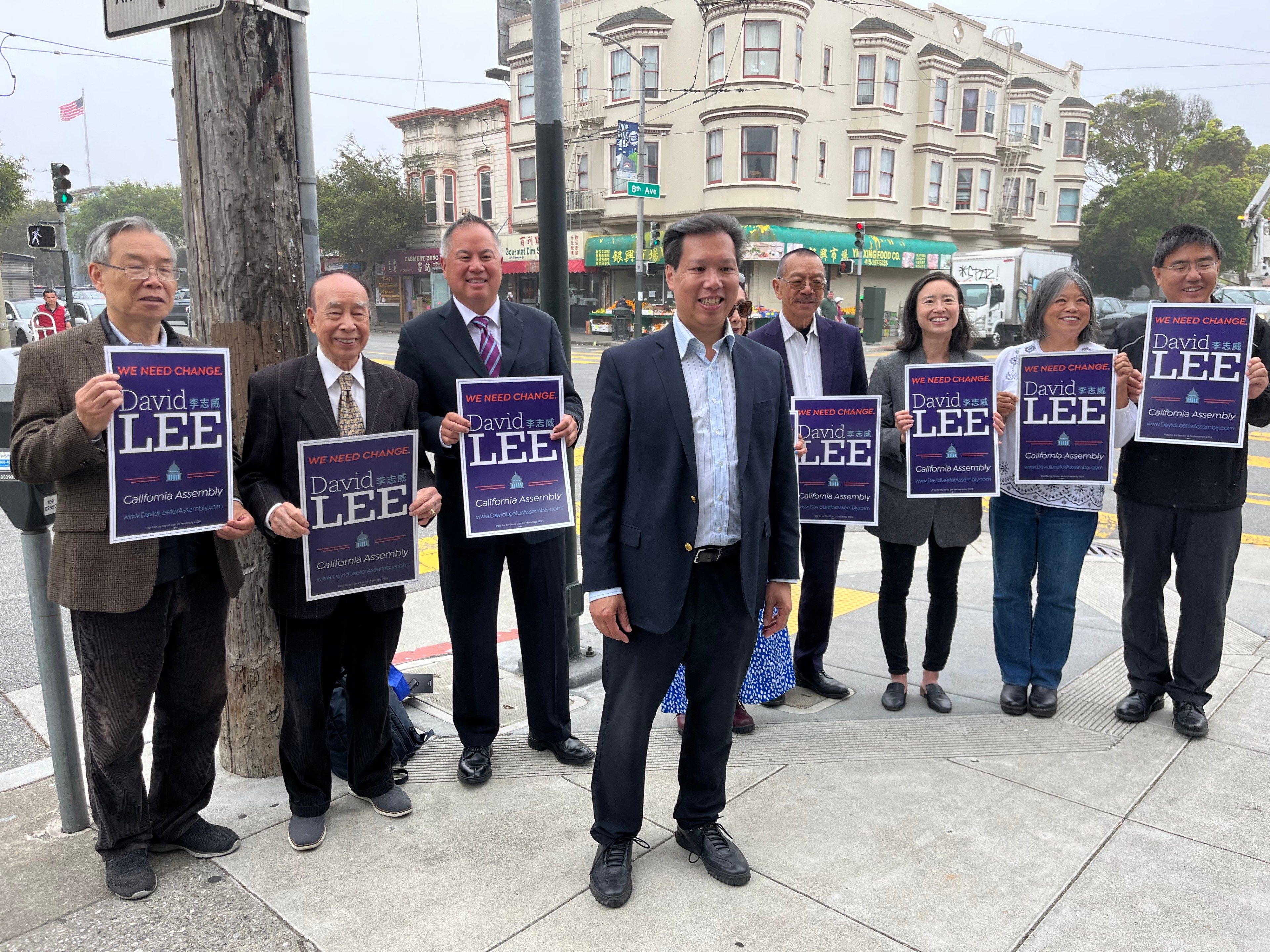 A group of people smiling, holding political campaign signs for David Lee for California Assembly, on a city street.