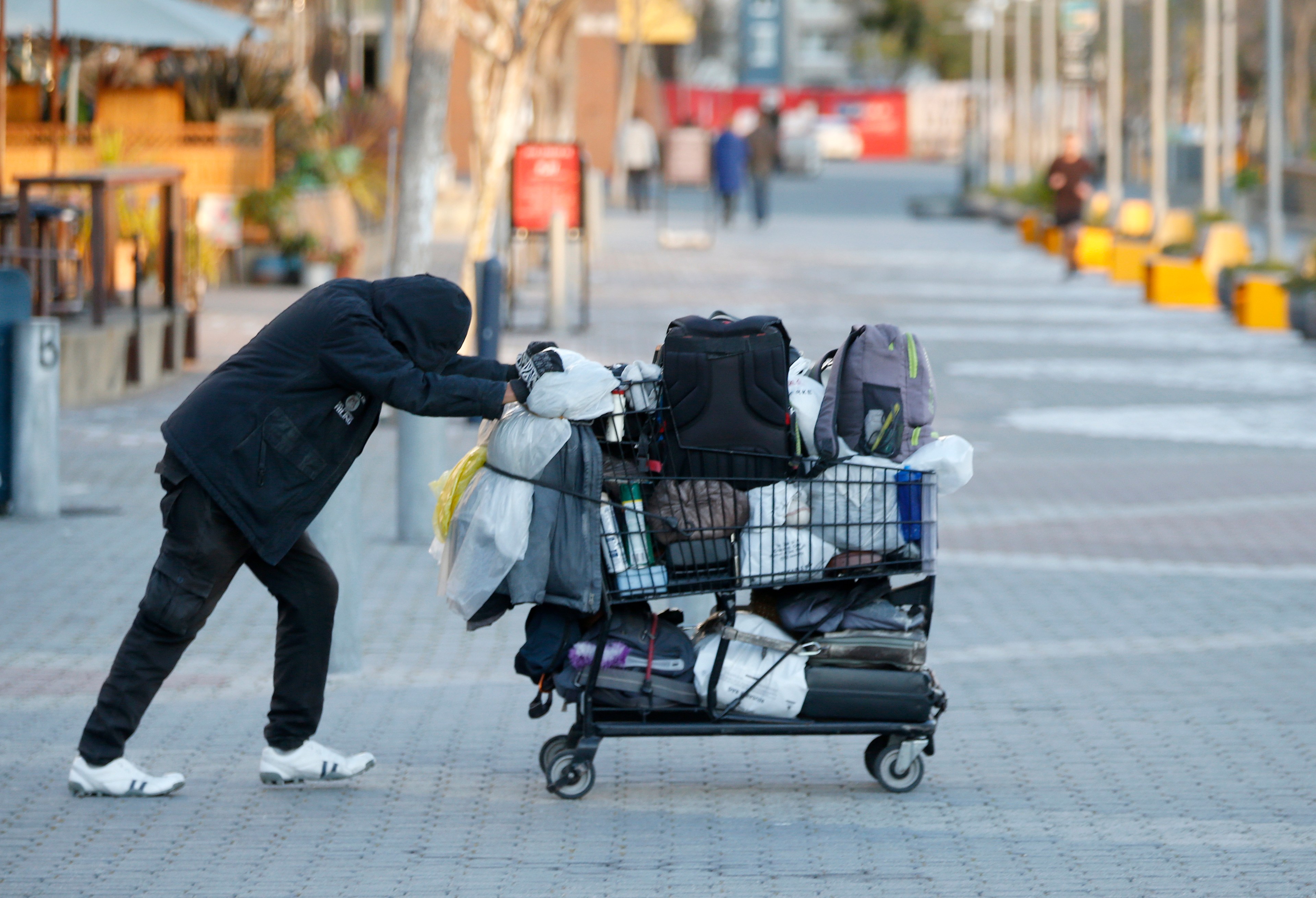 A man in black attire pushes a shopping cart full of belongings.