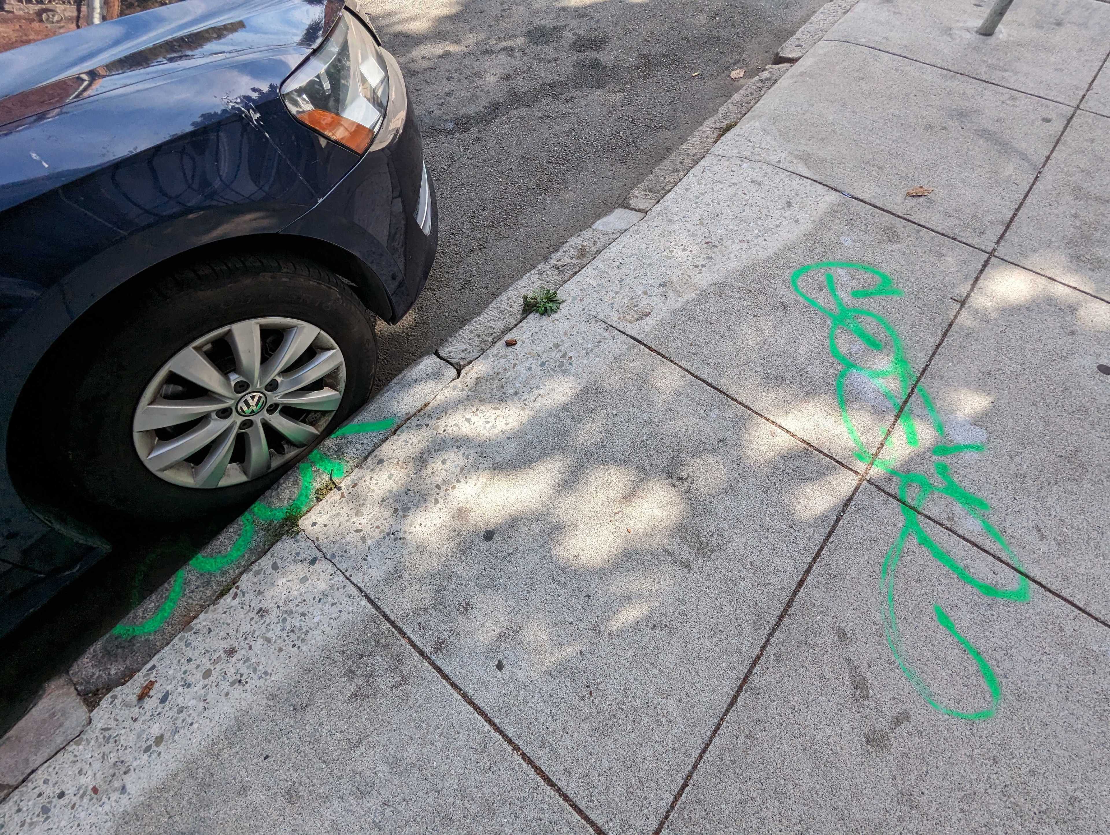 On a Langton Street sidewalk north of Folsom Street in San Francisco's South of Market neighborhood, two tags in fluorescent green spray paint mark a sidewalk and curb.